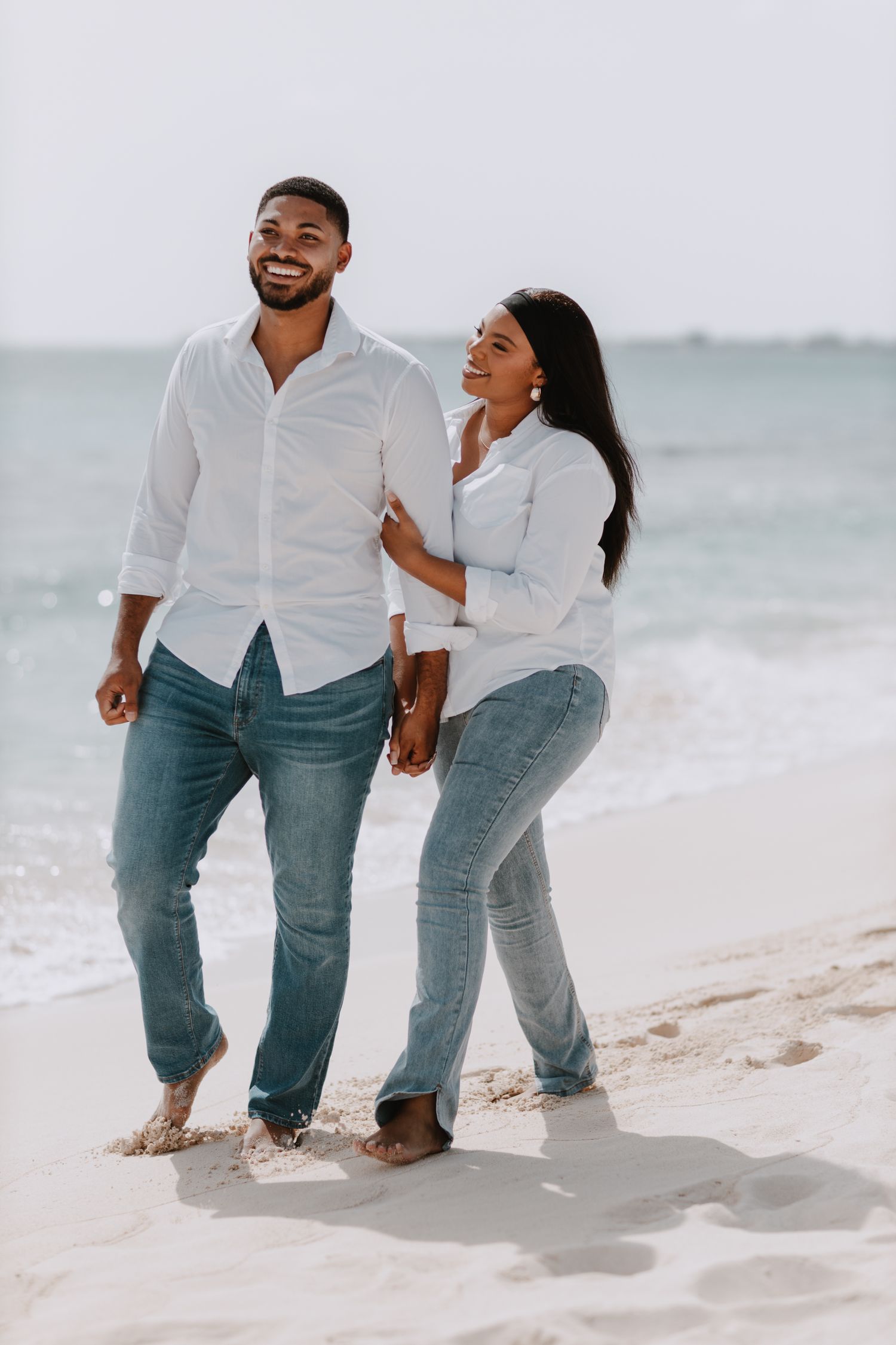 Casual couple walking and laughing together on white sandy beach.