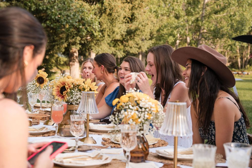 Women laughing and socializing at an outdoor garden party table adorned with sunflower centerpieces.