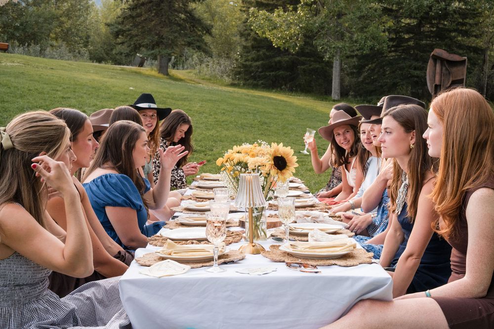 Women gathered around an outdoor dining table with sunflowers, enjoying an al fresco garden party on a sunny day.