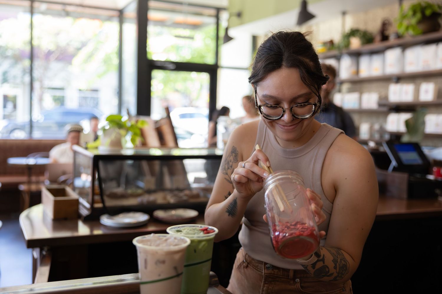 Someone in glasses enjoys a refreshing drink while sitting at a cafe counter in natural lighting.