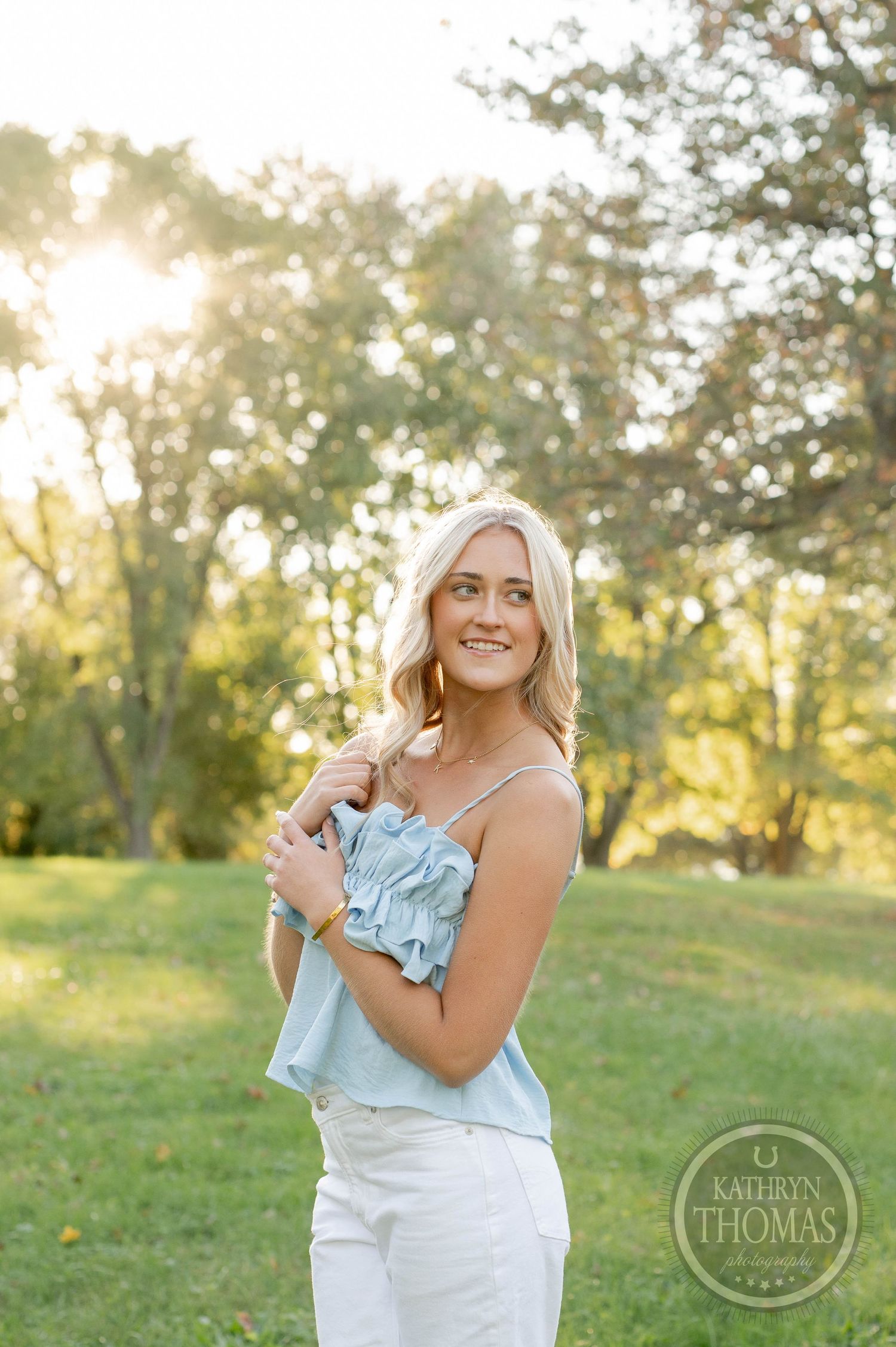 Portrait of someone wearing blue sleeveless top smiling in natural outdoor setting at sunset.