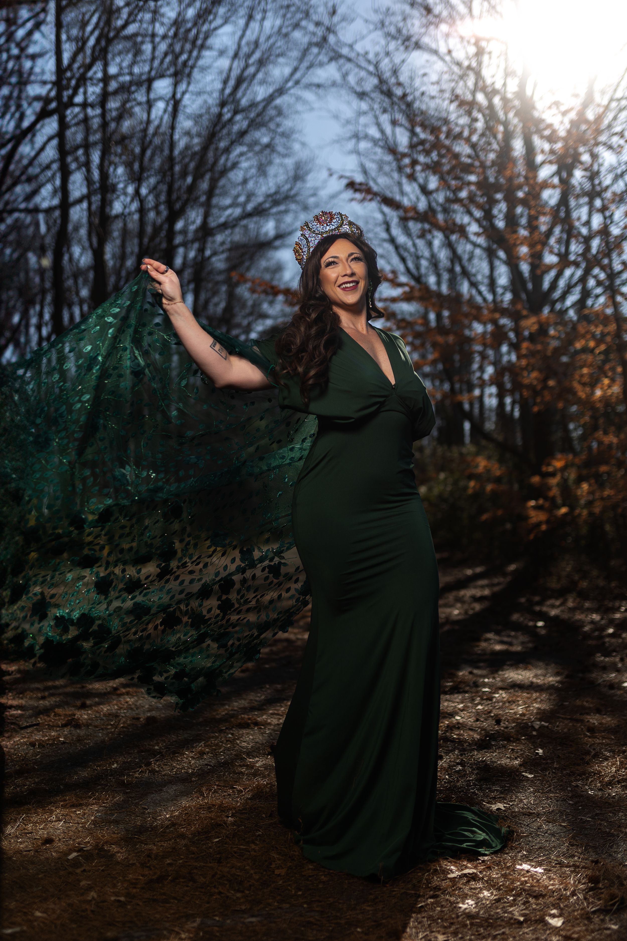 Elegant emerald green gown with flowing cape captured in moody forest setting during golden hour.