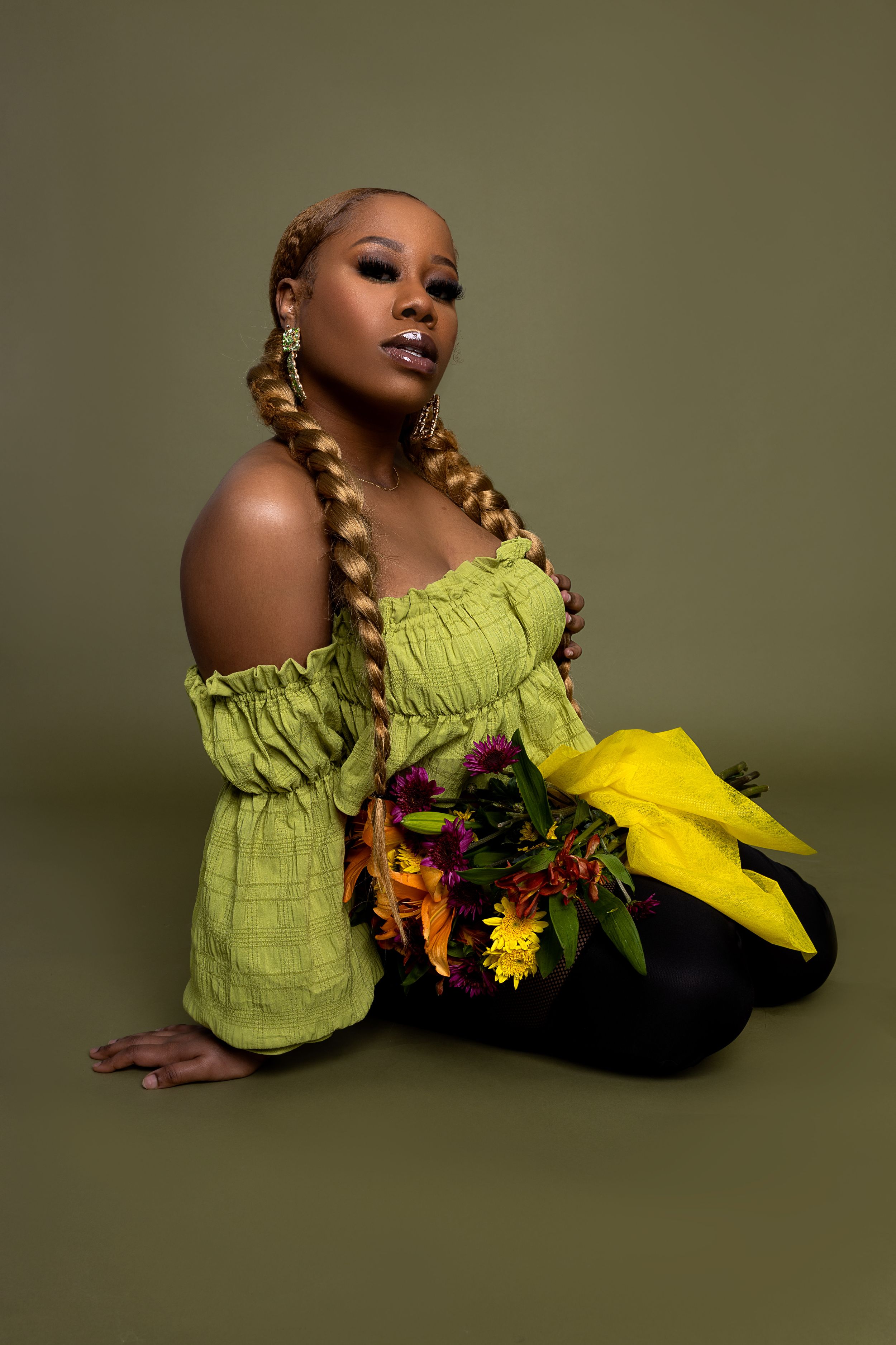 Artistic fashion portrait with green off-shoulder top and yellow florals against olive backdrop.