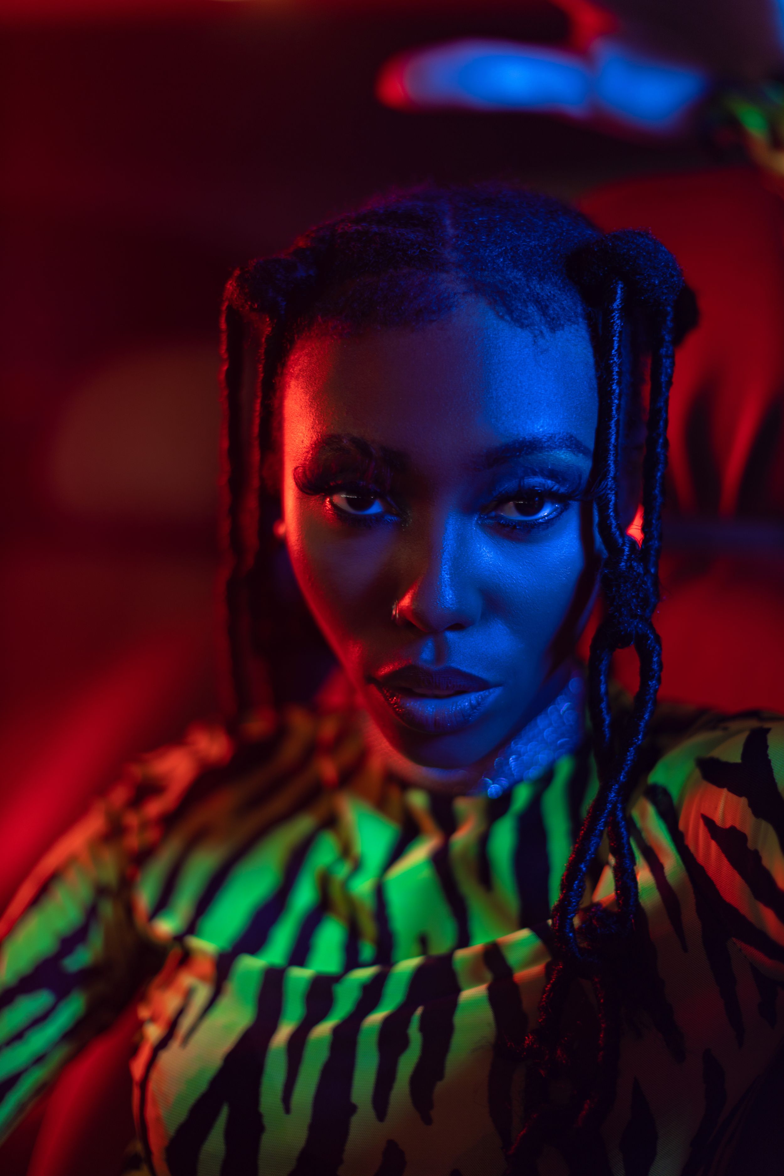 Colorful portrait with dramatic red and blue lighting casting shadows on figure wearing zebra print in nightclub setting.