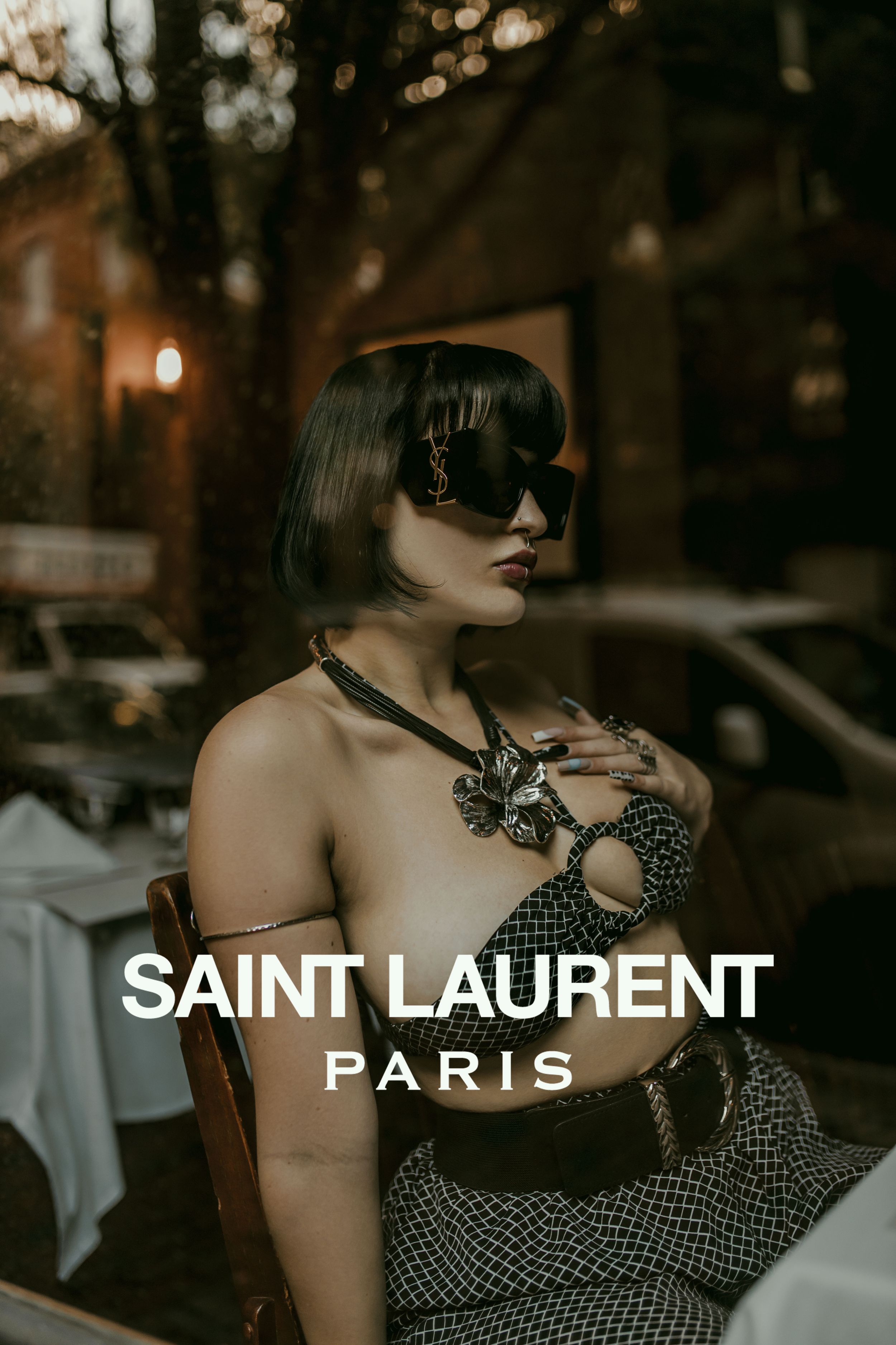 Fashion advertisement for Saint Laurent Paris featuring model in sunglasses and polka dot dress in moody evening setting.