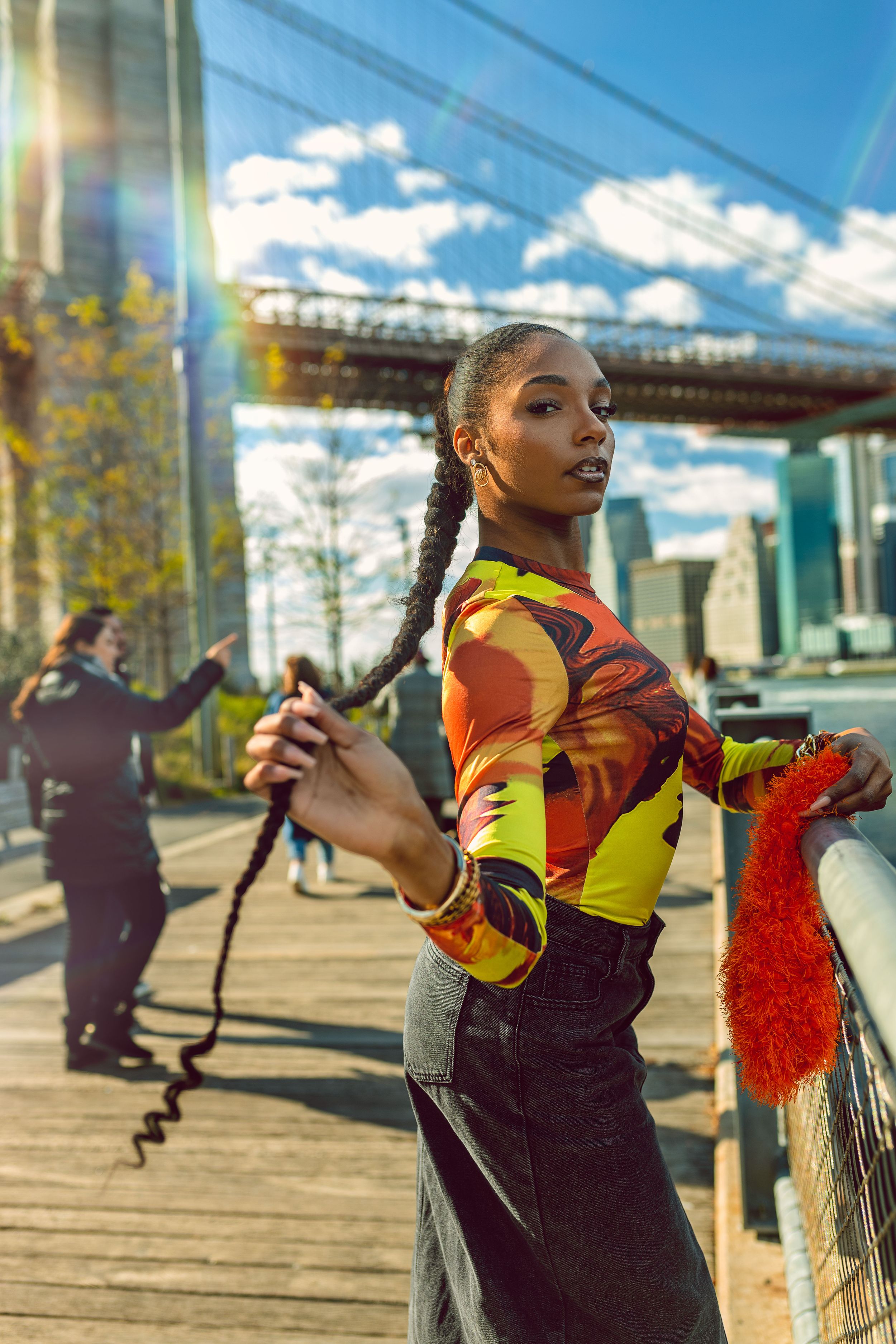 Athletic figure in bright colorful activewear poses on a waterfront path with bridge and city skyline in background.