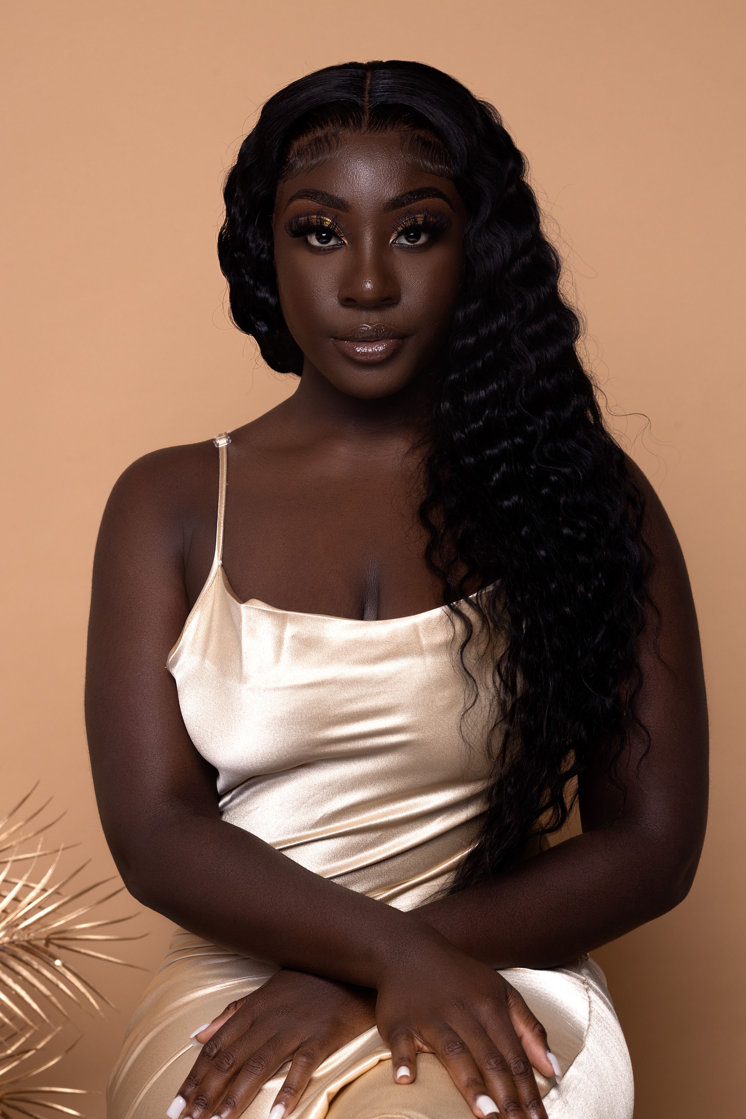 Portrait of person wearing white satin camisole against warm brown background with palm leaves.