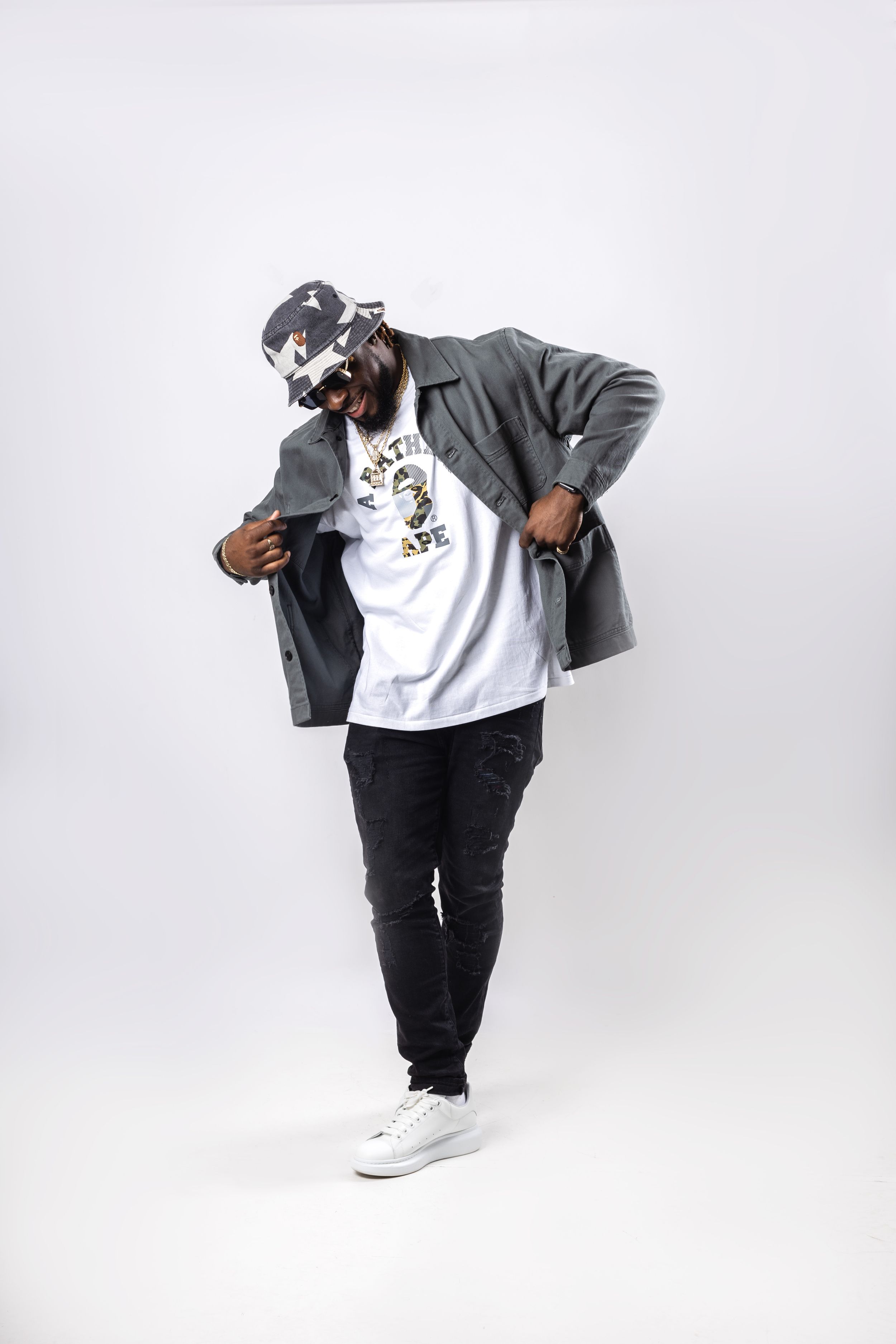 Person in casual urban wear with gray jacket, white t-shirt and black pants strikes a stylish pose against white backdrop.