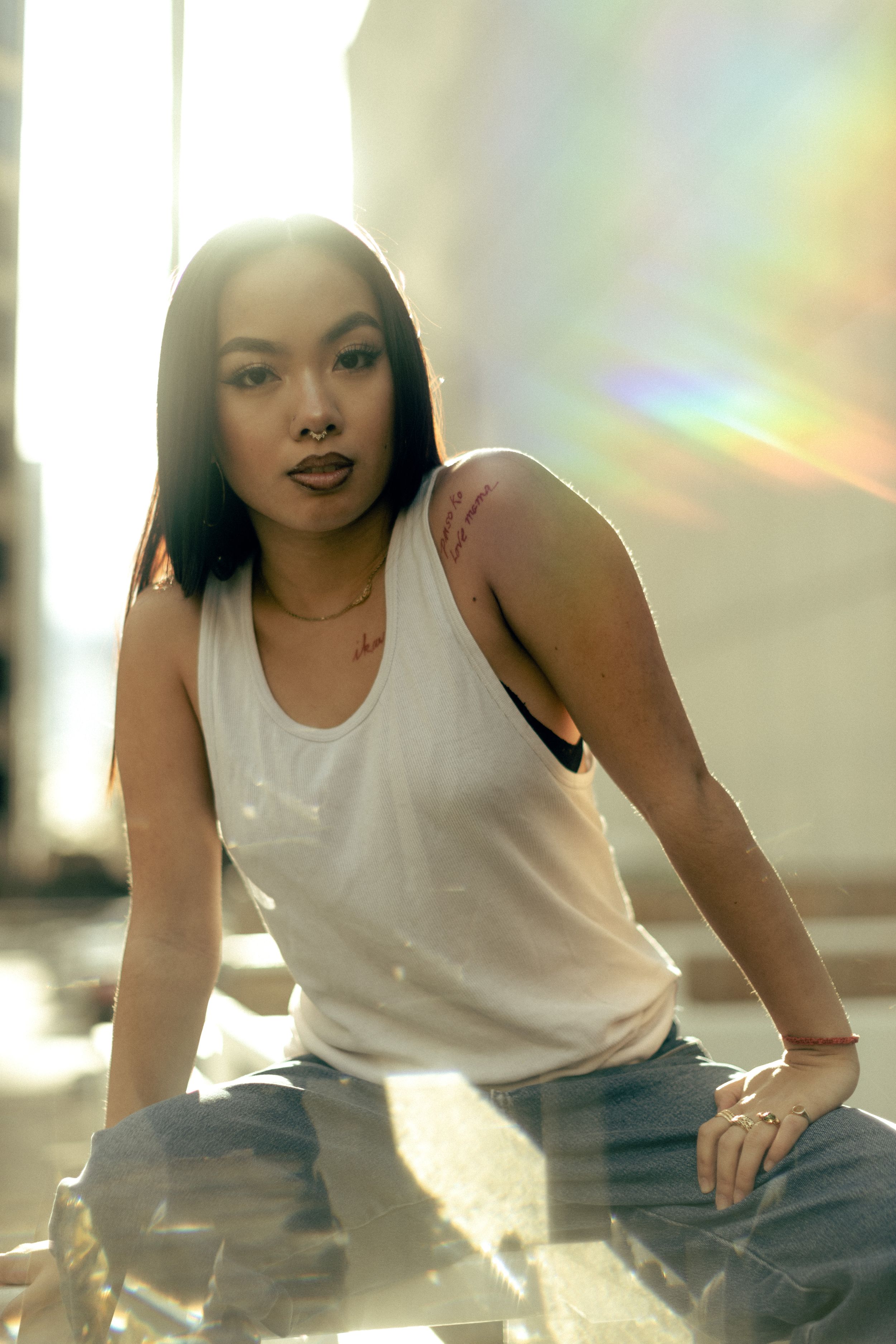 Stylish portrait photo with holographic backdrop and lens flare featuring white tank top and denim in soft lighting.
