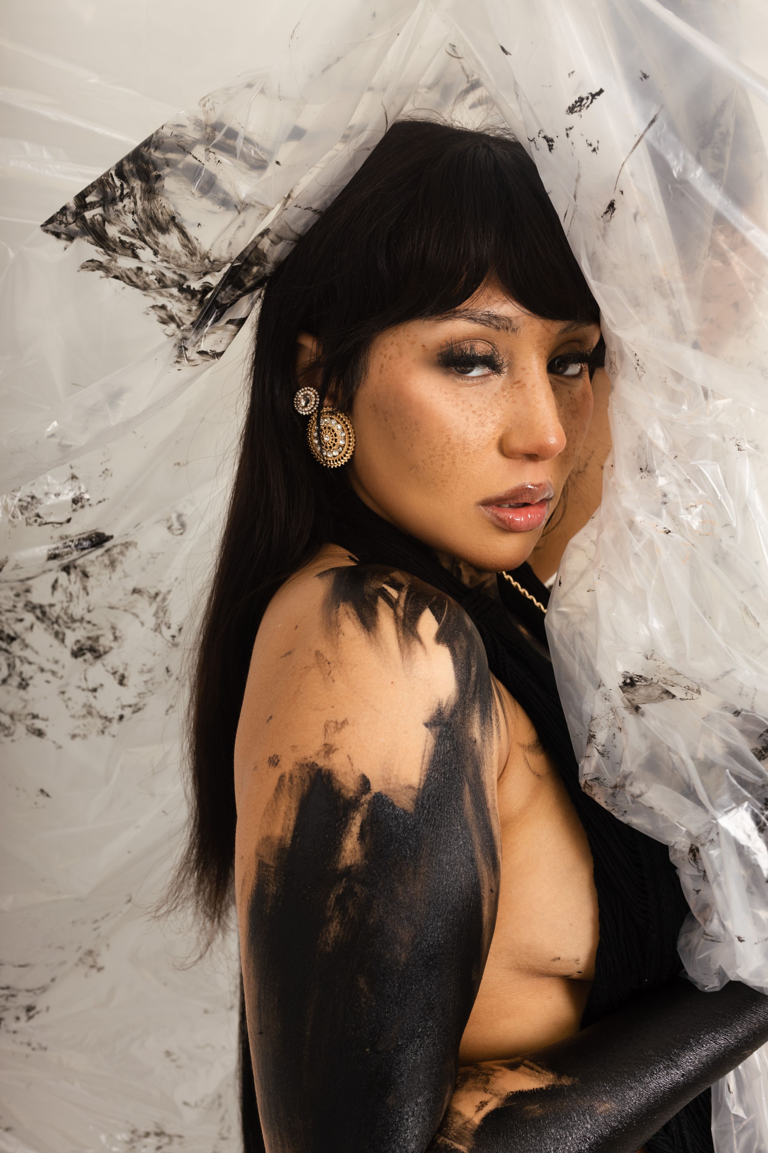 Artistic portrait with dramatic black paint effects on skin against white tulle fabric backdrop.