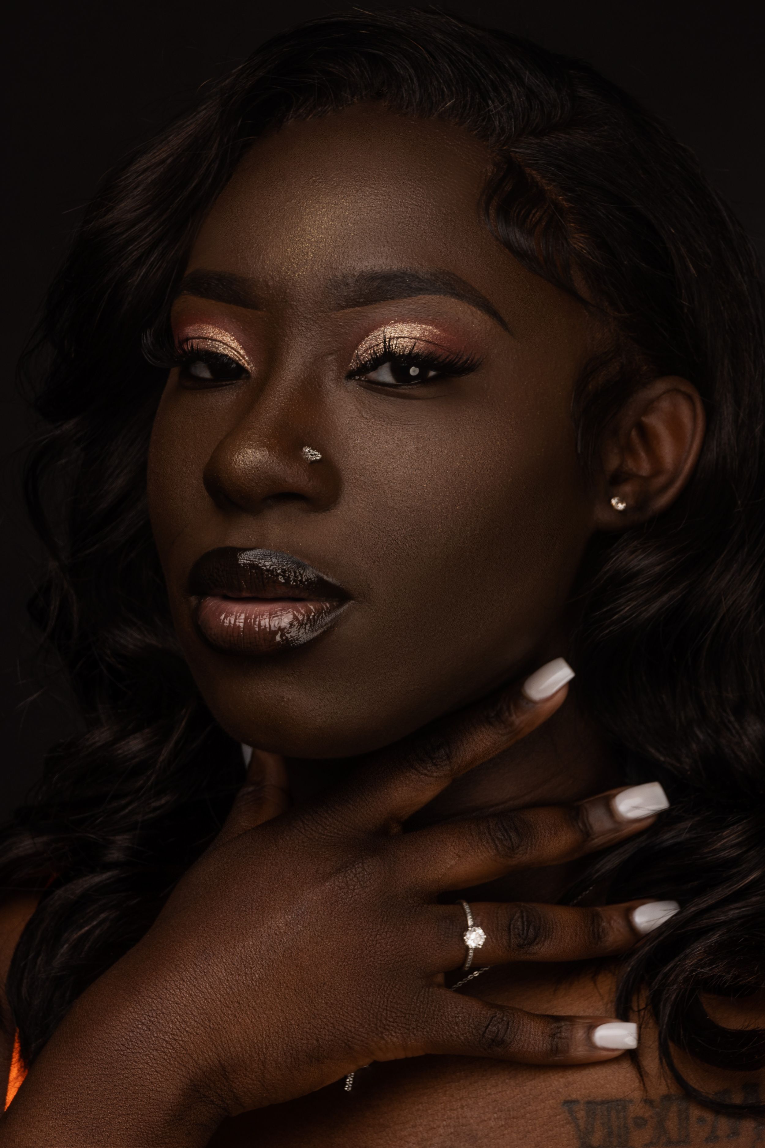 Dramatic beauty portrait with shimmering bronze eyeshadow, white manicure and ring against dark background.