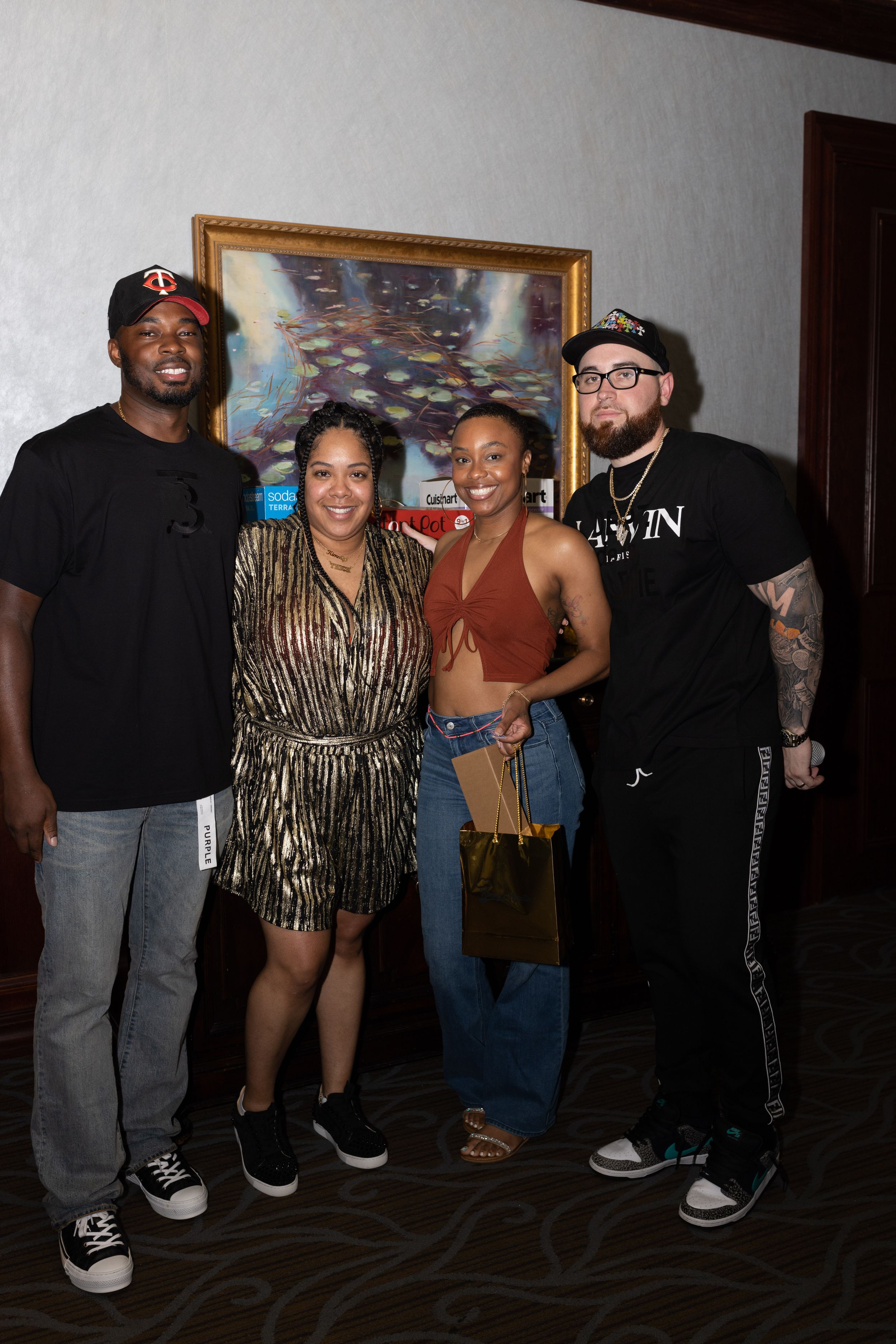 Four people pose together for a group photo in front of a framed artwork on a wall.