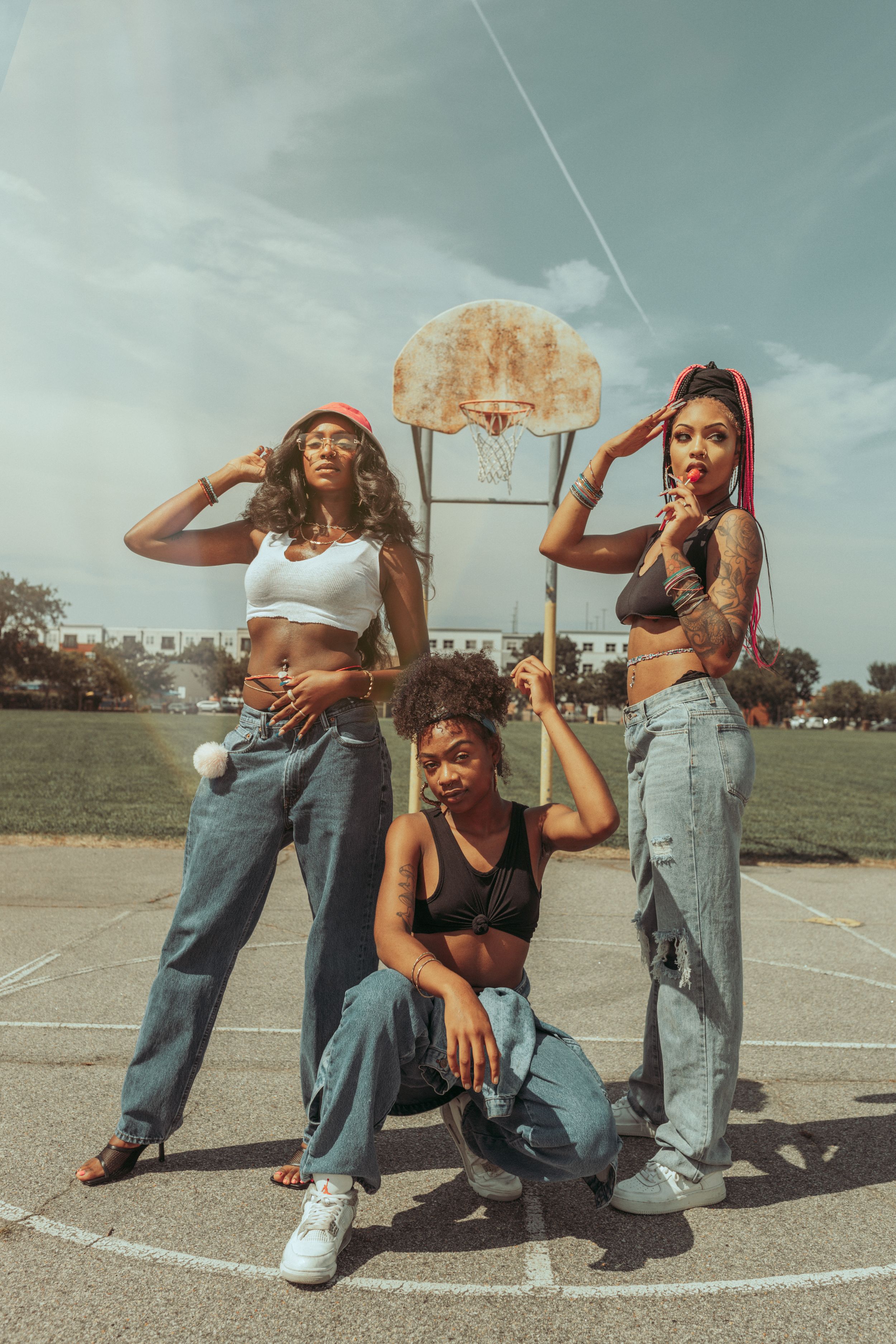 Friends pose together on an outdoor basketball court on a sunny day wearing casual 90s style clothing and crop tops.