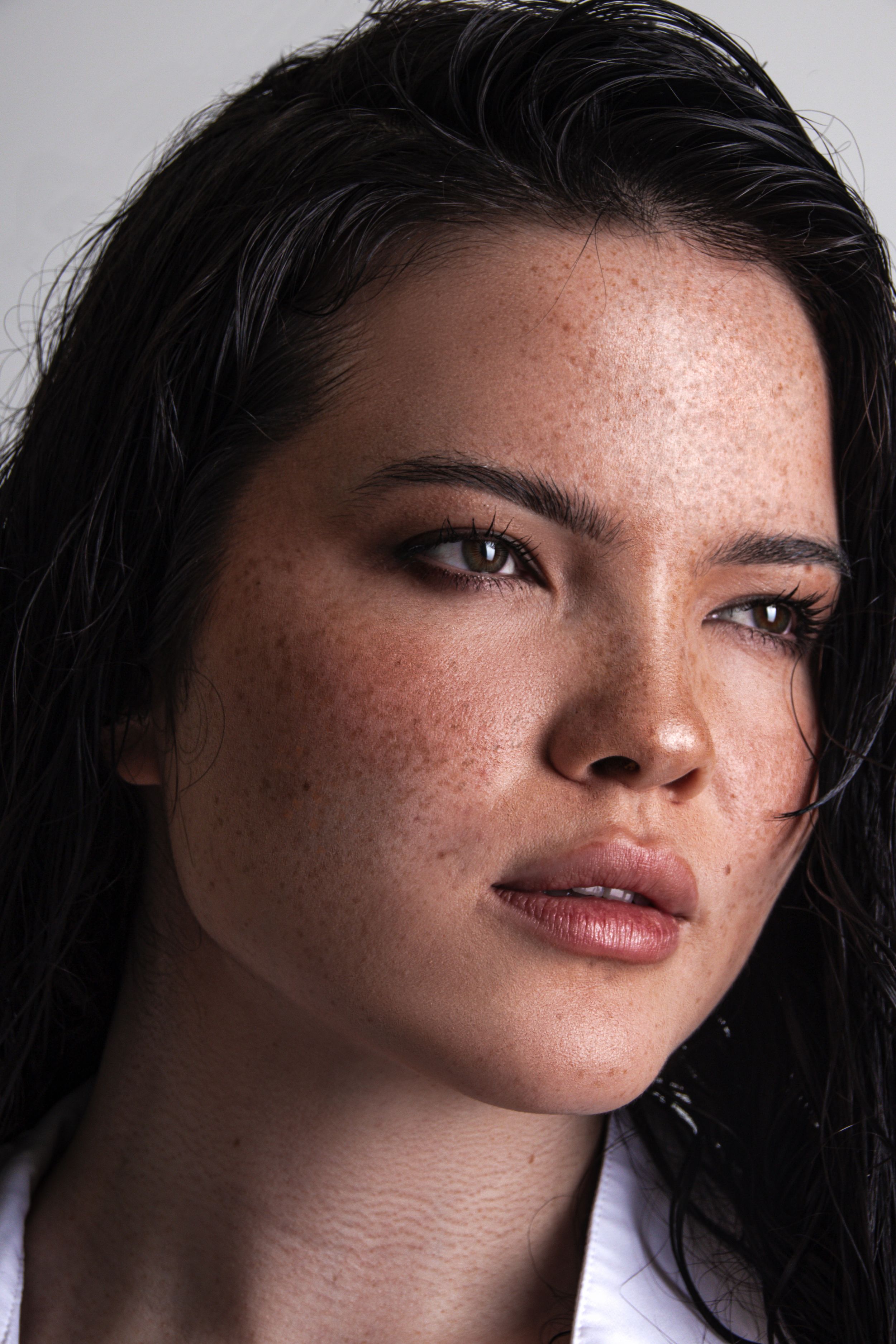 Close-up beauty portrait showing natural skin texture and long dark hair against light background.