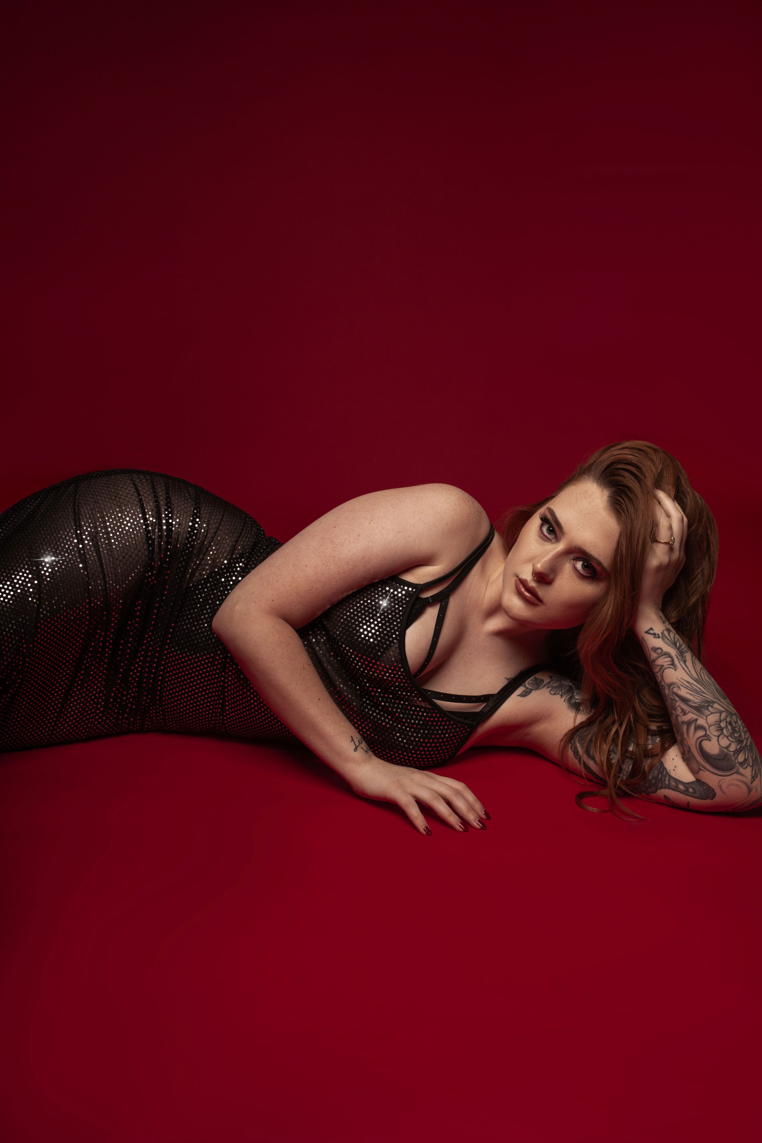 Figure in sequined dress poses elegantly against deep red backdrop in glamorous studio photoshoot.