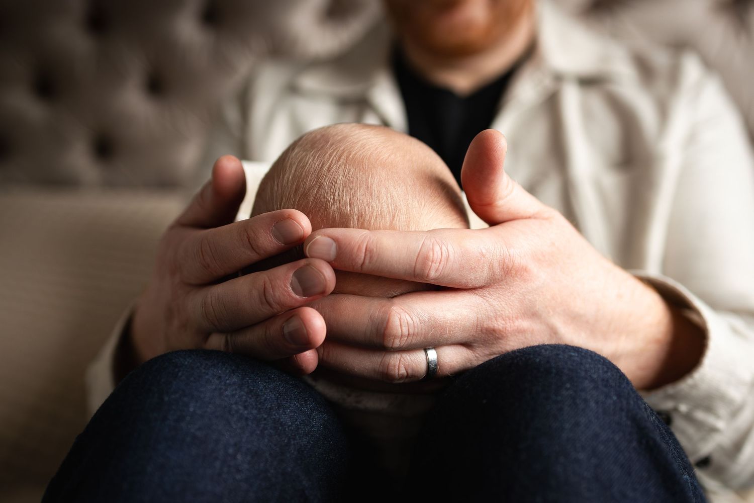 Close-up shot of hands folded together on lap while sitting on tufted furniture.