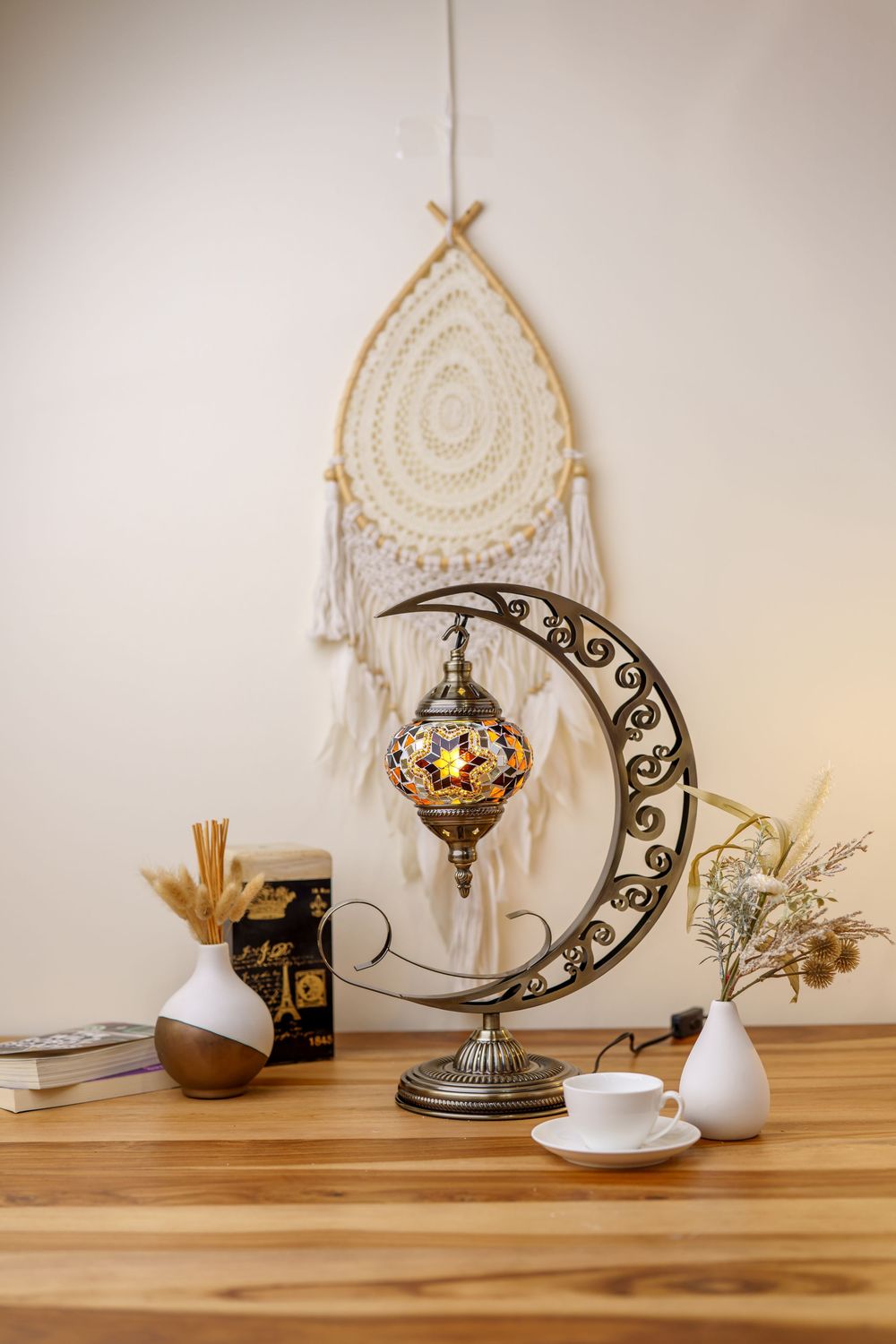 Bohemian crescent moon lamp with mosaic glass shade displayed with dreamcatcher and minimalist decor on wooden table.