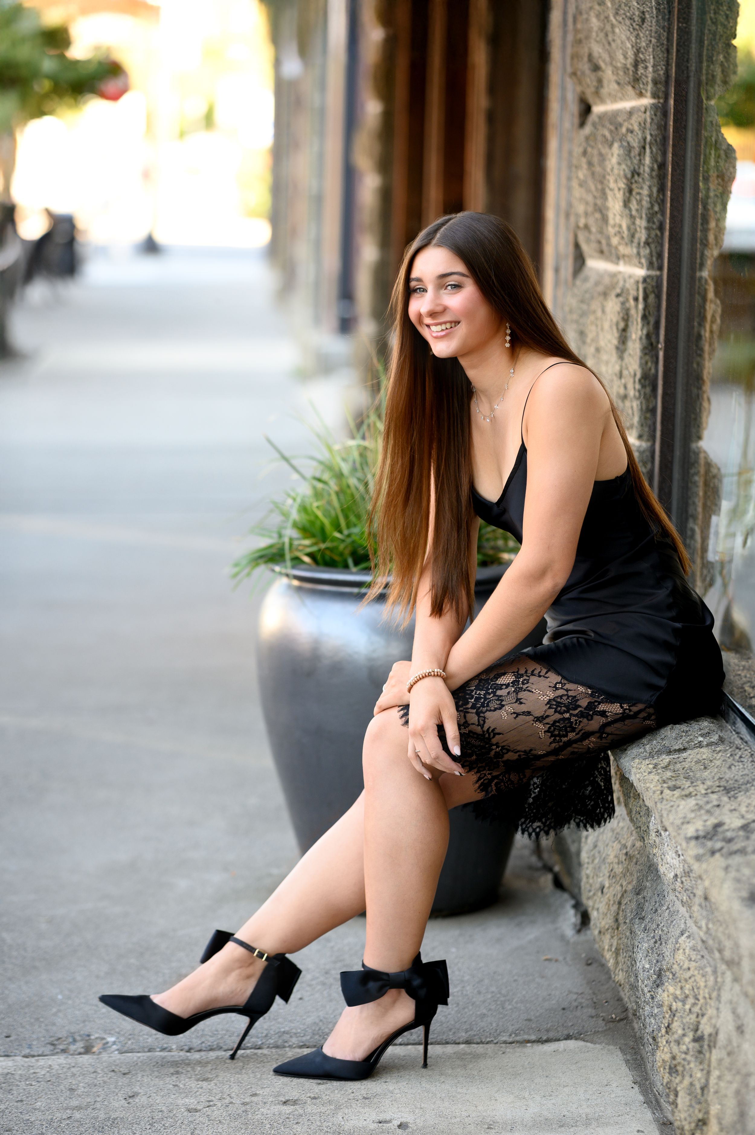 Person in black dress sitting on stone wall beside decorative planter.