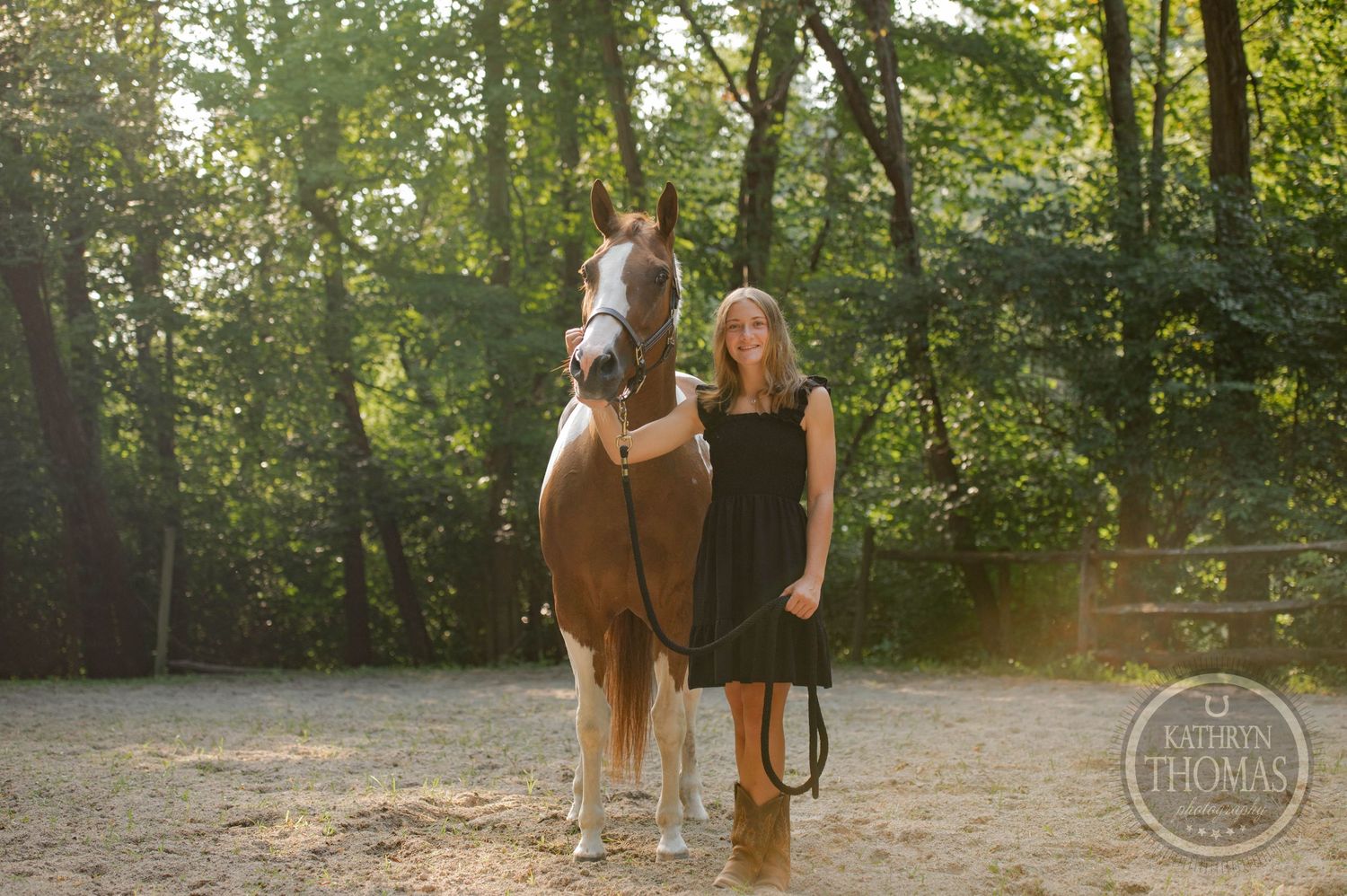 Person in black dress standing with chestnut horse in wooded setting.