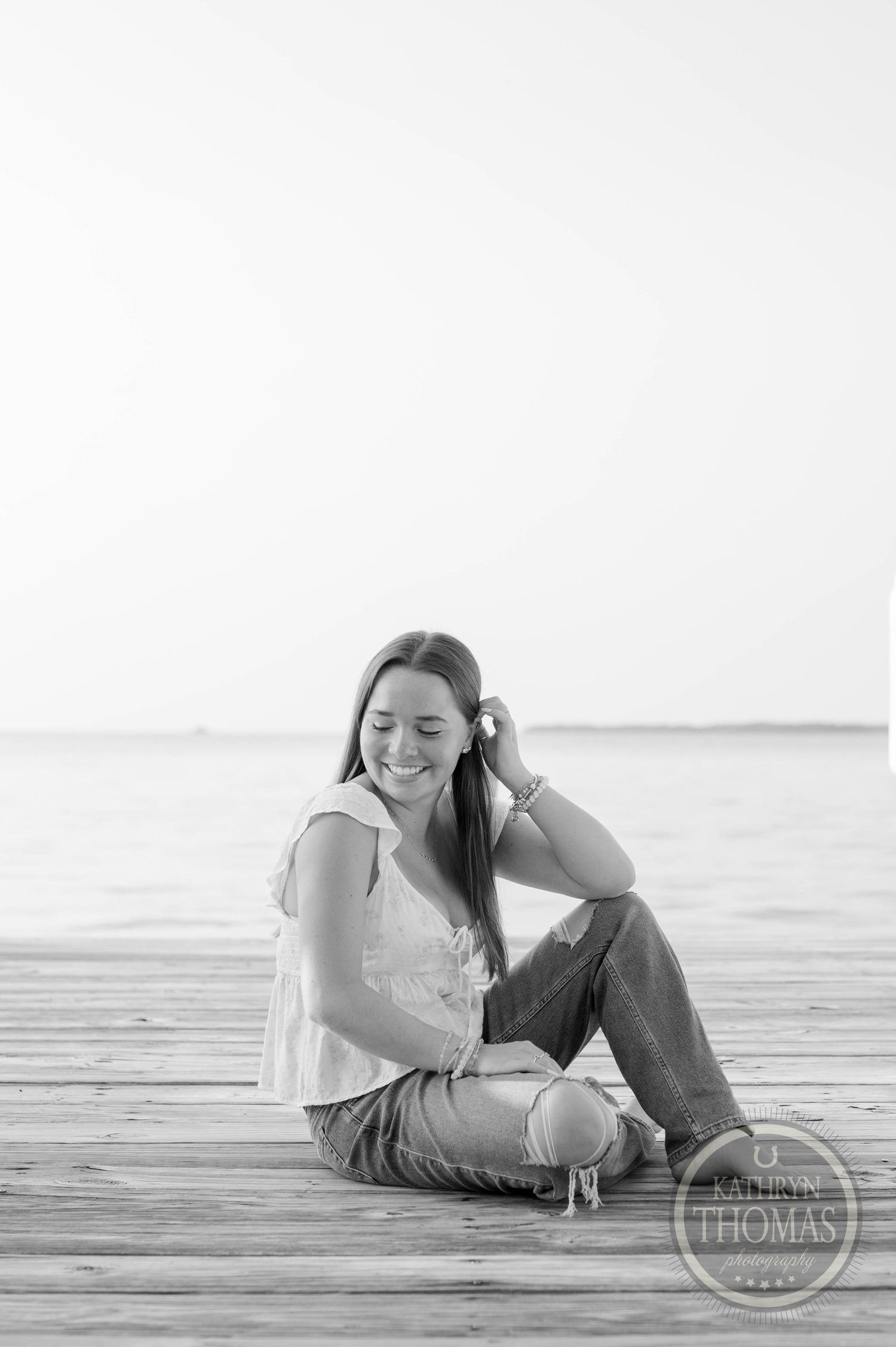 Black and white portrait of person sitting on dock by water.