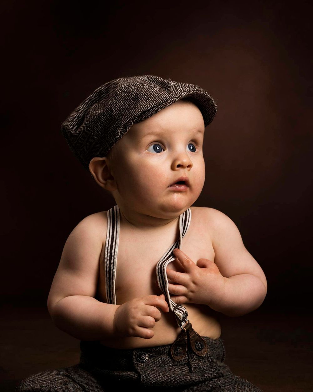 Portrett av baby i sixpence og bukseseler som holder seg på magen under en babyfotografering hos fotograf i Lyngdal