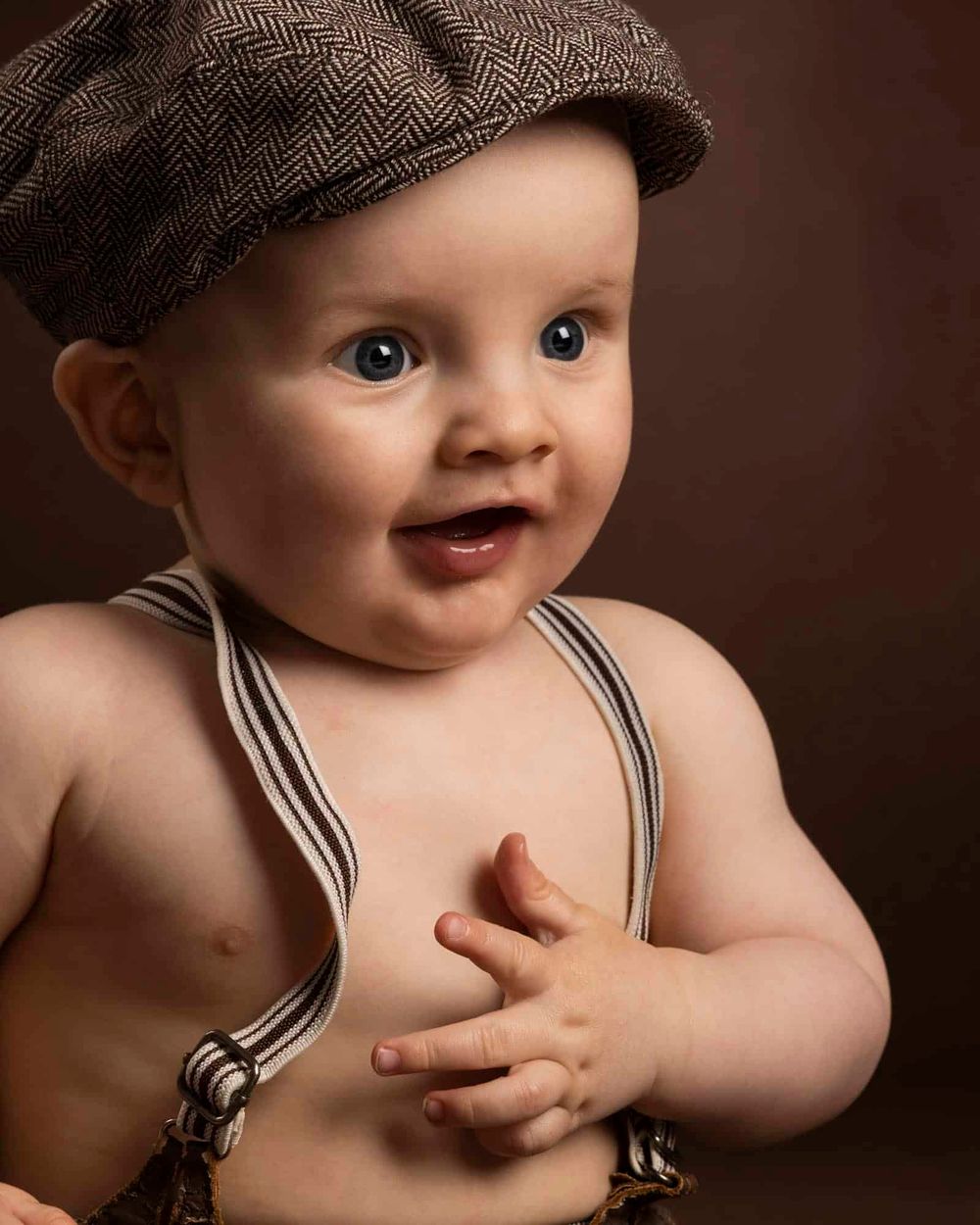 Portrett av baby i sixpence og bukseseler som holder seg på magen og smiler under en babyfotografering hos fotograf i Lyngdal