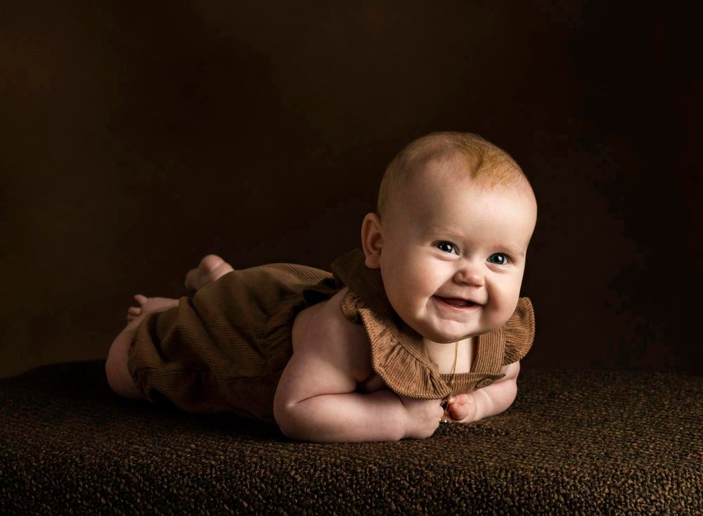 Baby på 5 mnd ligger på magen og smiler under en babyfotografering i et fotostudio i Lyngdal