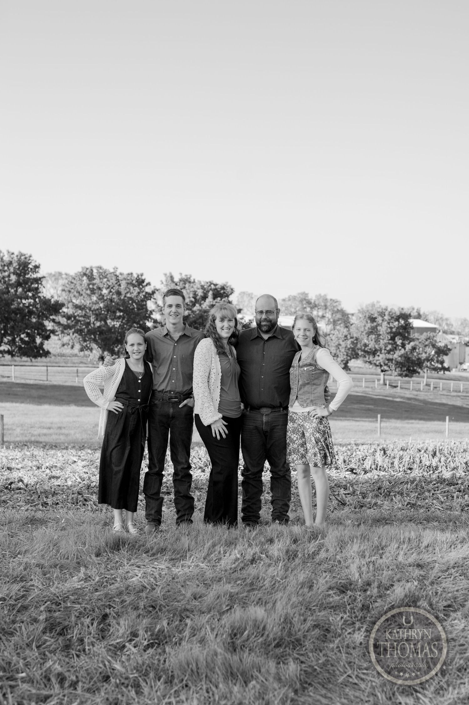 Black and white family portrait of five people in a countryside setting.
