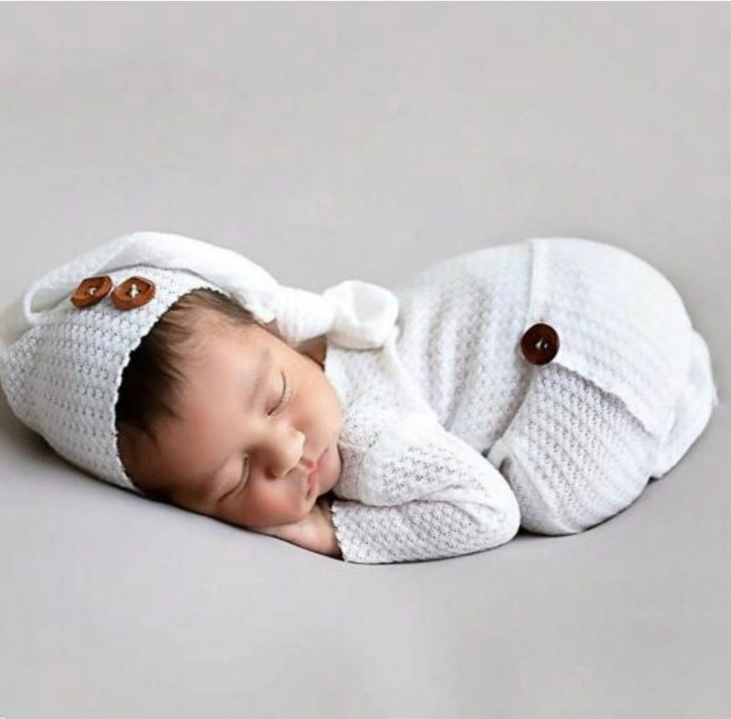 Sleeping baby wrapped in white knit blanket with wooden button details.