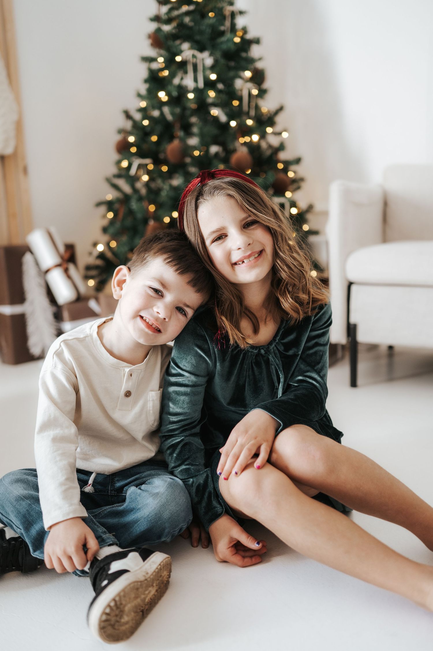 Children sitting together on the floor during Christmas with decorated tree and lights in the background.