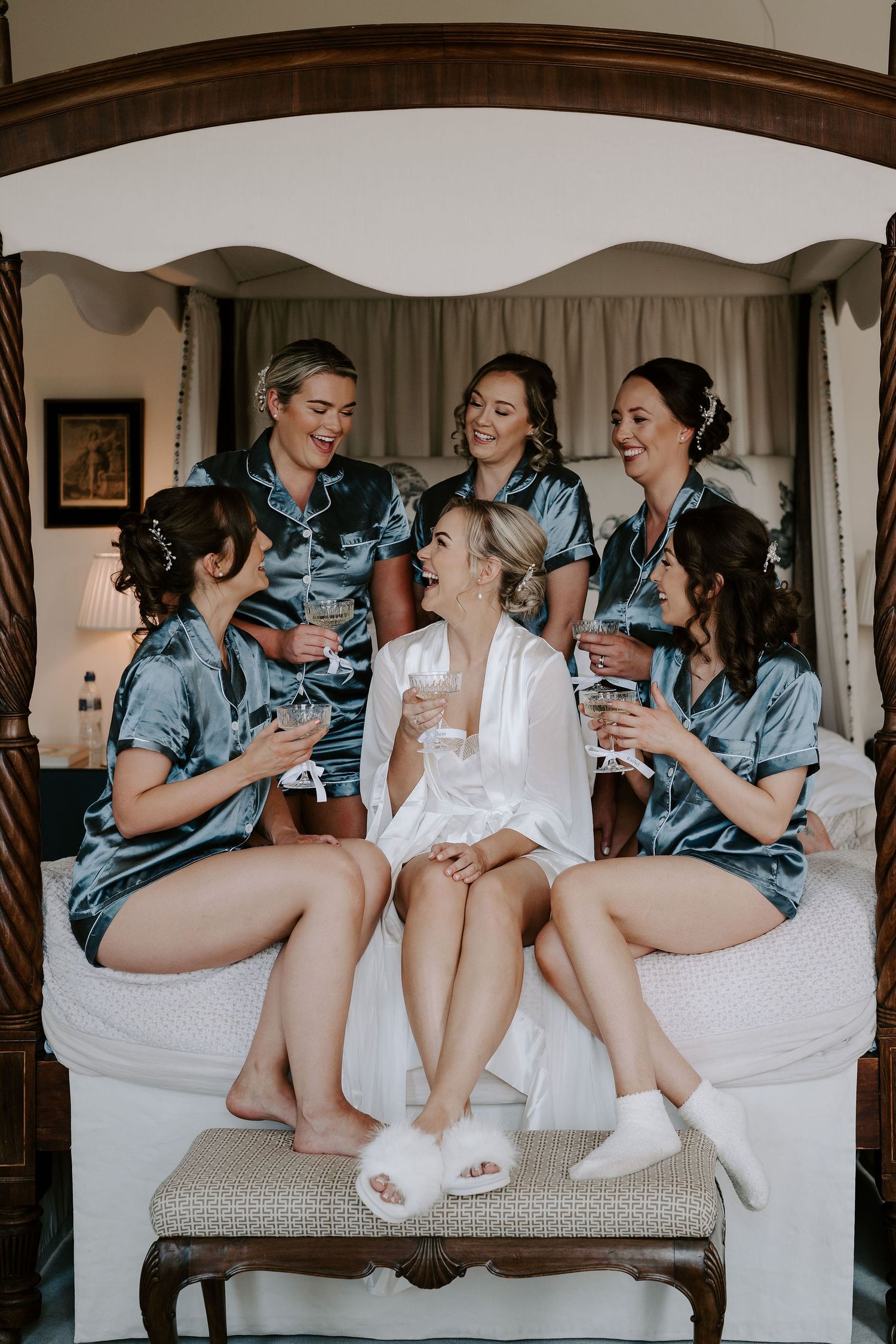 bride and bridesmaids drinking champagne sat on the bed at Iscoyd park