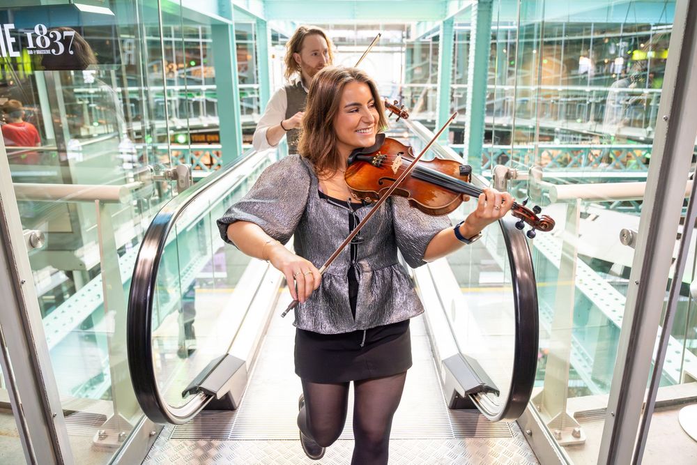 Musician performs on violin while standing near an escalator in the Guinness Storehouse, Dublin.