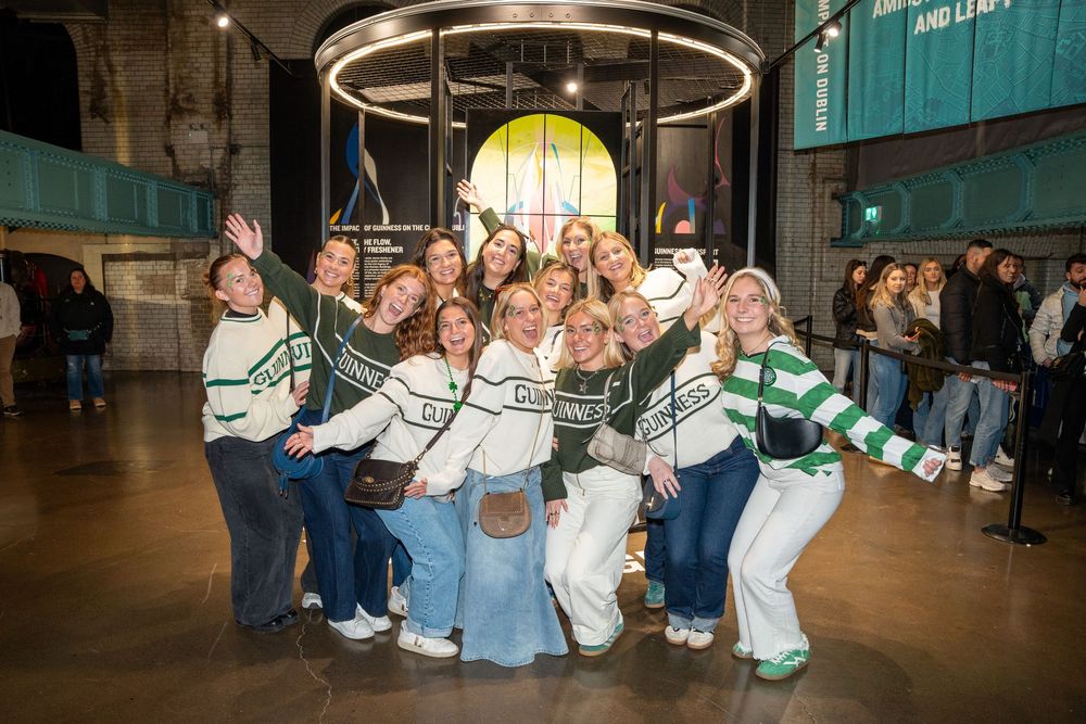A group wearing matching Guinness jumpers poses together enthusiastically at The Guinness Storehouse, Dublin.