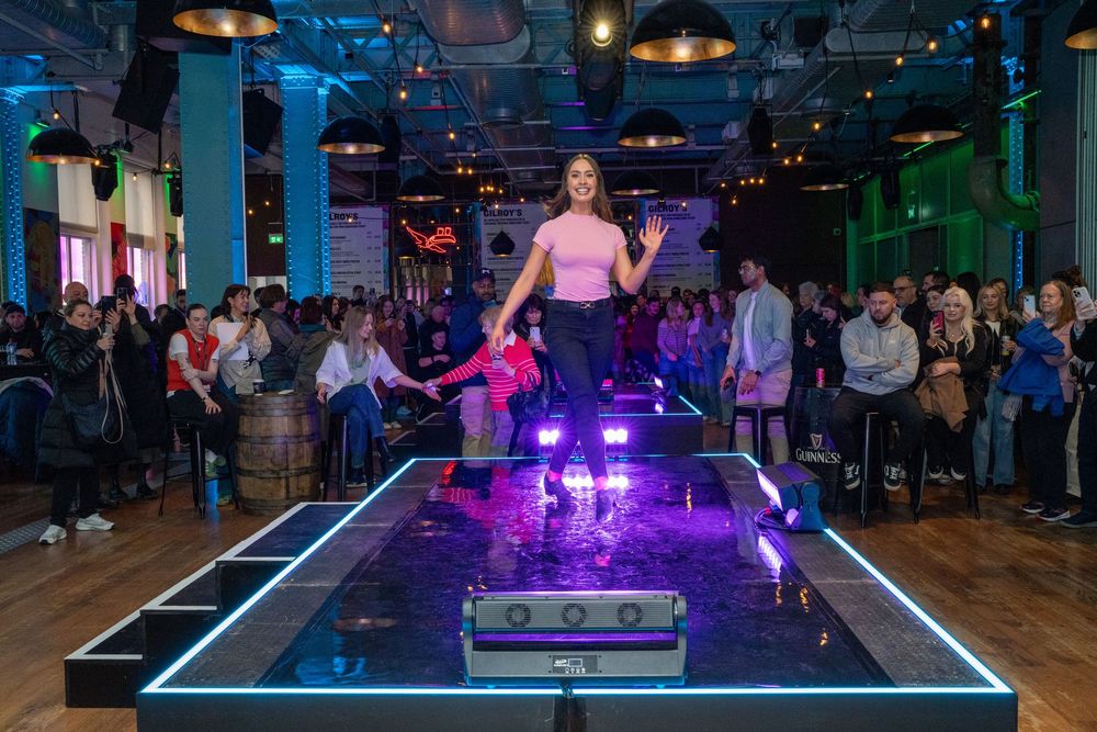 Dimly lit indoor venue with blue and purple lighting showing a dance floor with crowd silhouettes.