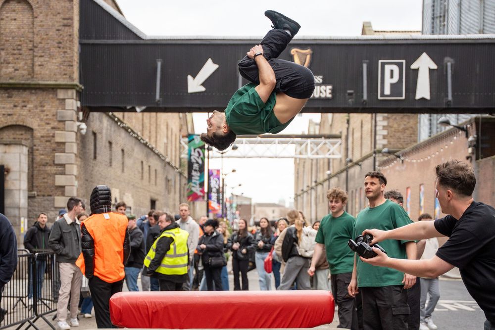 An athlete performs a backflip over a red mat while spectators watch at The Guinness Storehouse, Dublin.