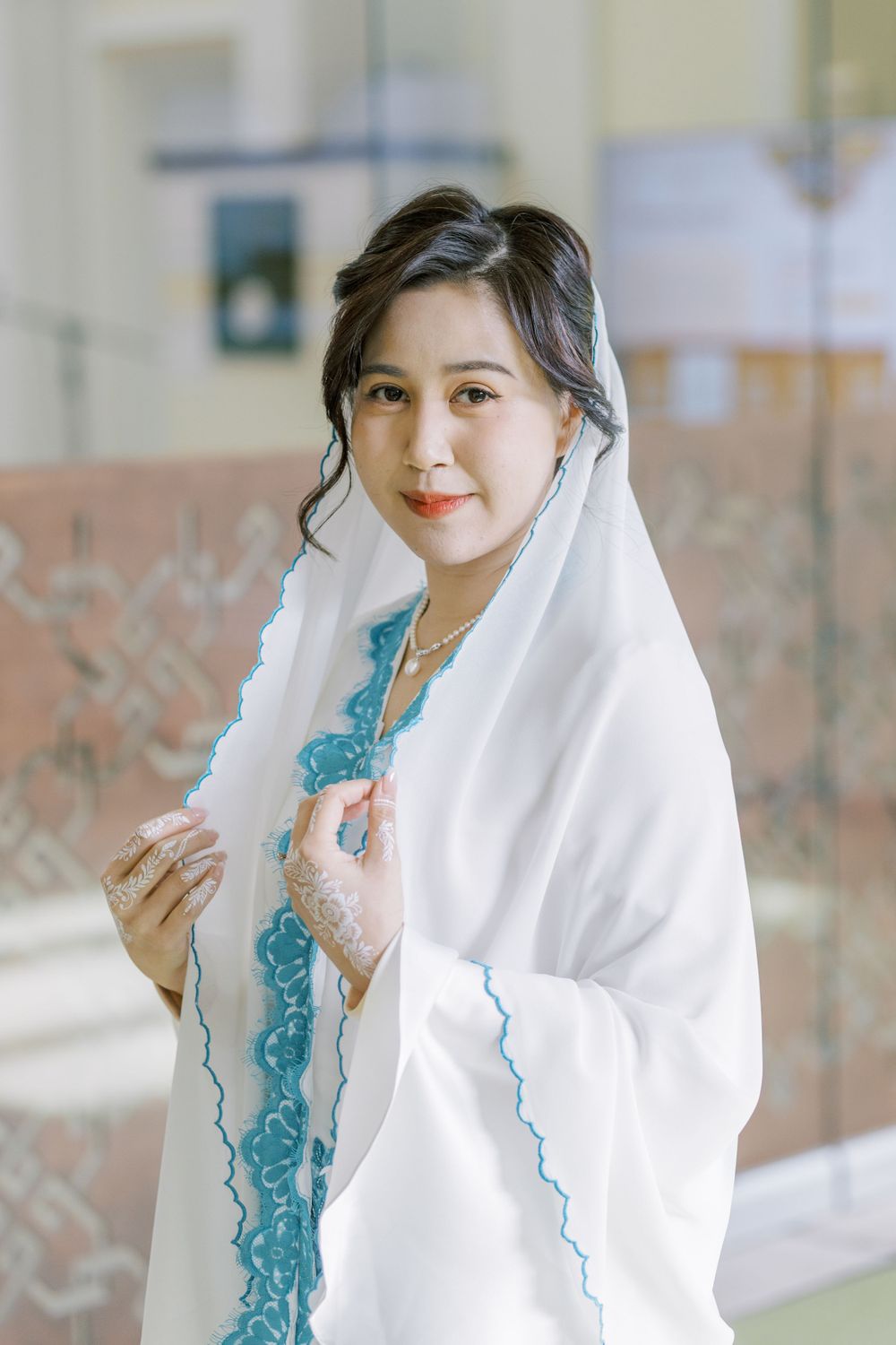 A person in a white shawl and blue dress poses elegantly in a hallway.
