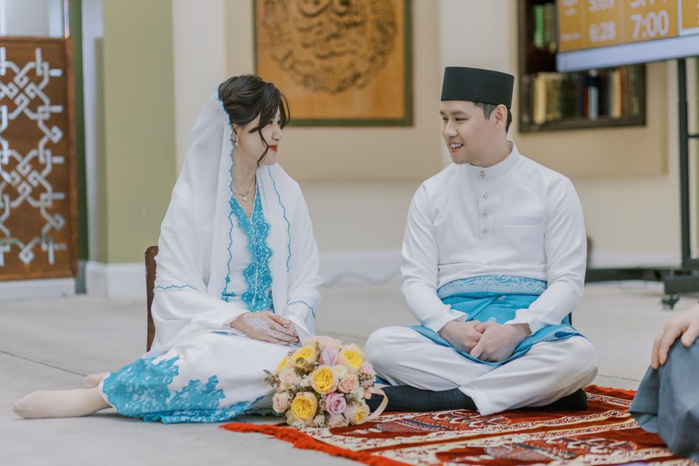 Indoor photoshoot scene with couple in traditional dress sitting on decorative rug.