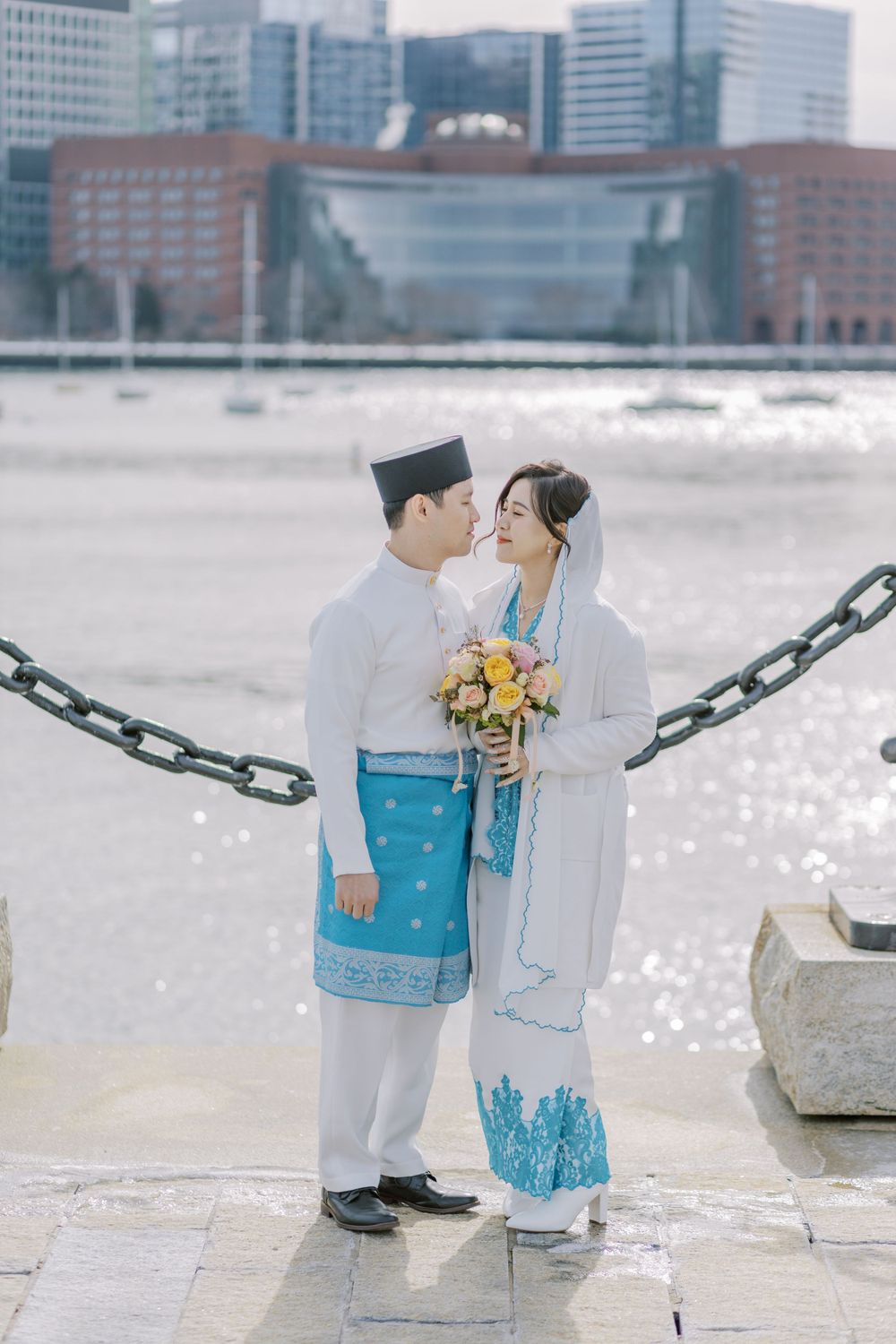 Miniature wedding couple figurines posed against urban waterfront backdrop.
