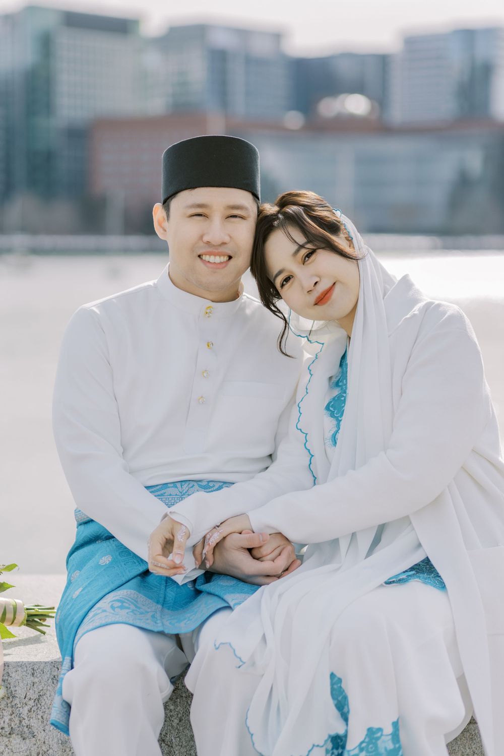 A couple in white and turquoise outfits pose together outdoors in a romantic photoshoot setting.