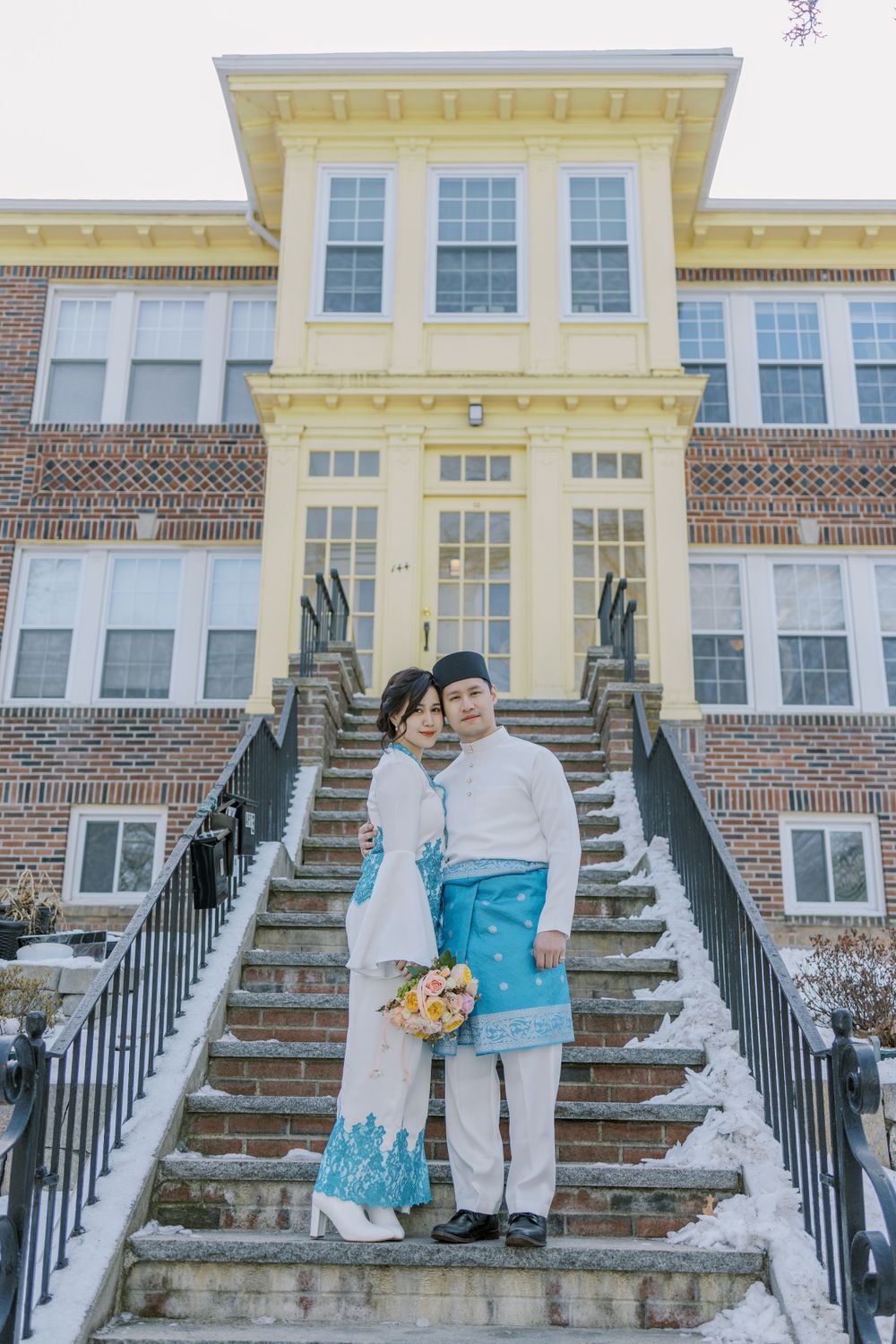 Couple poses on brick building steps in coordinated traditional white and blue outfits.
