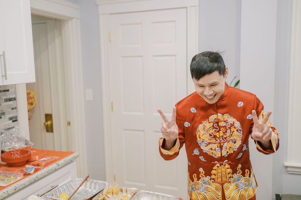 Person in red traditional Chinese attire making peace signs at camera in kitchen setting.