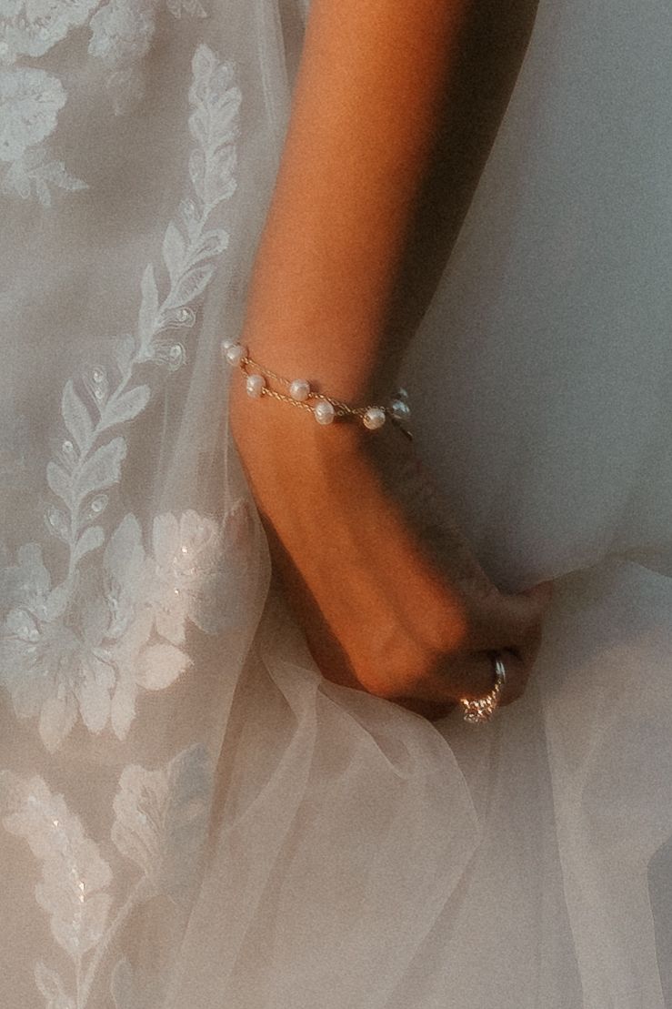Close-up view of delicate pearl bracelet and engagement ring against white lace fabric background.