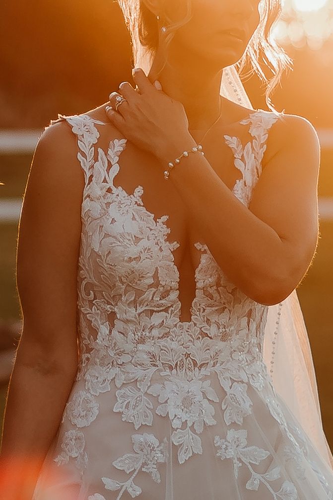 Close-up details of delicate white lace floral appliques on a wedding dress bodice in warm sunset lighting.