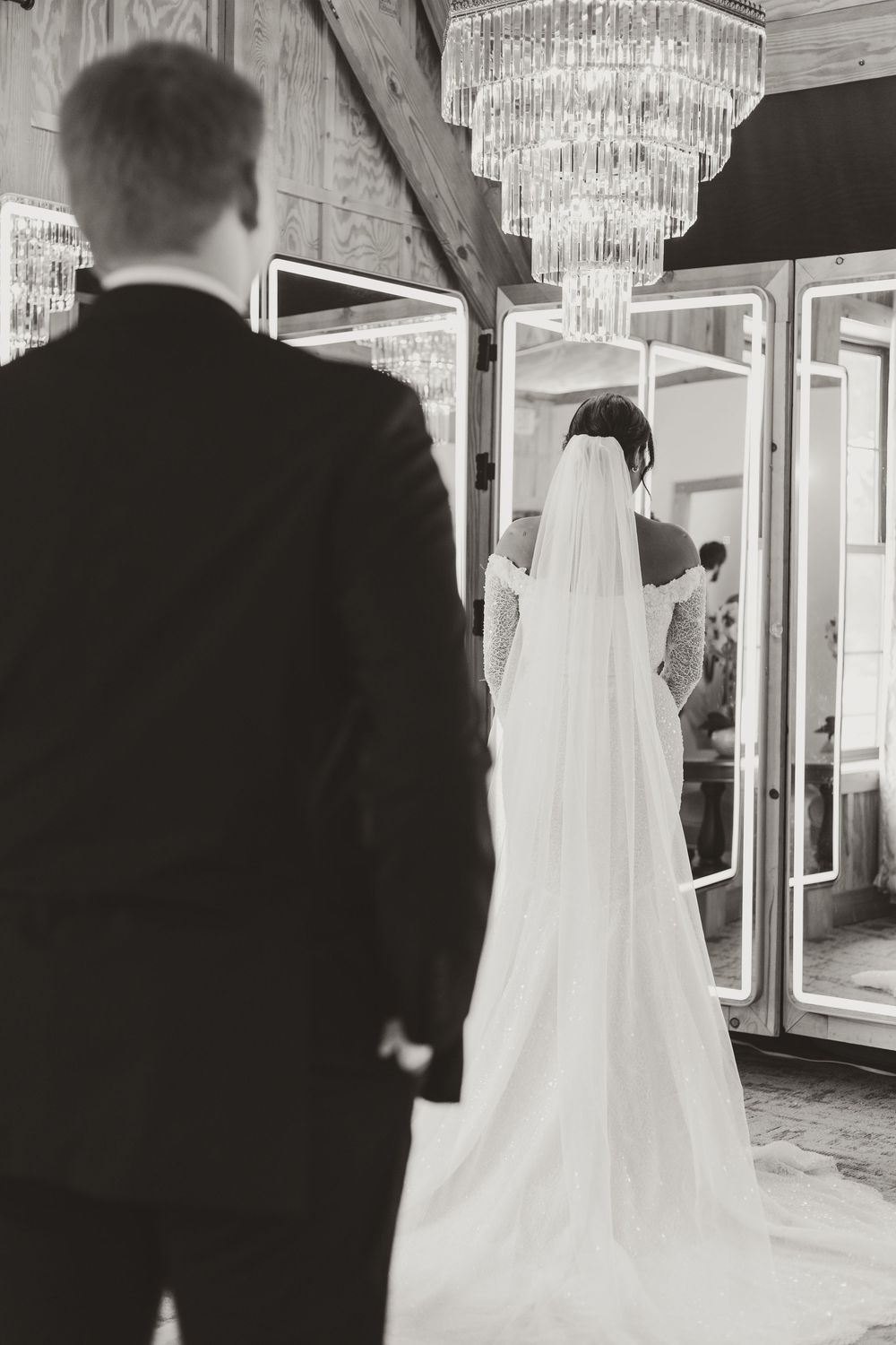 A wedding couple walking under crystal chandeliers in an elegant venue hallway.