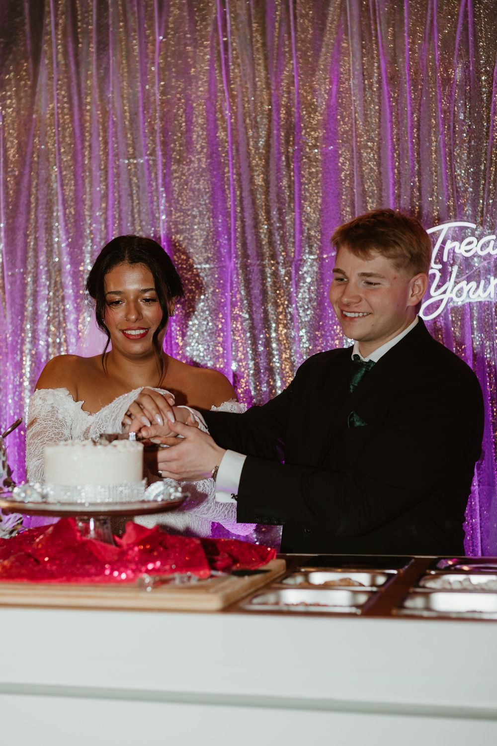Wedding reception scene with sparkly pink backdrop and guests seated at decorated tables.
