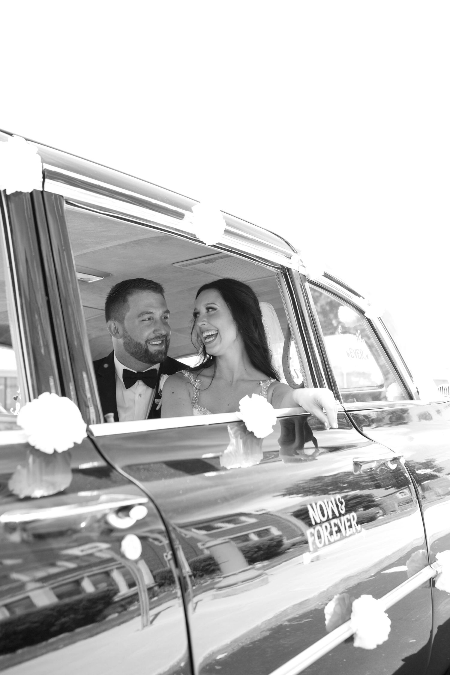 Happy newlyweds share a joyful moment while sitting in a classic car decorated with flowers for their wedding day.