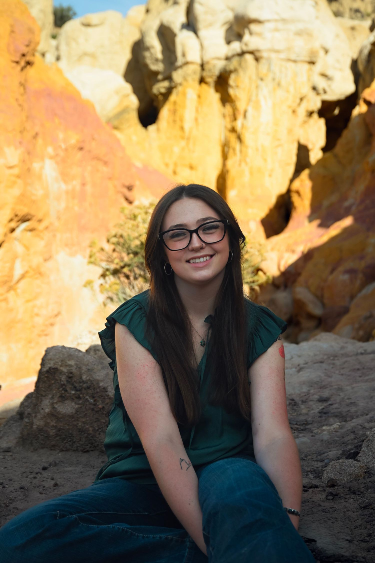 Young woman with glasses in green dress sitting among vibrant orange and red rock formations outdoors.
