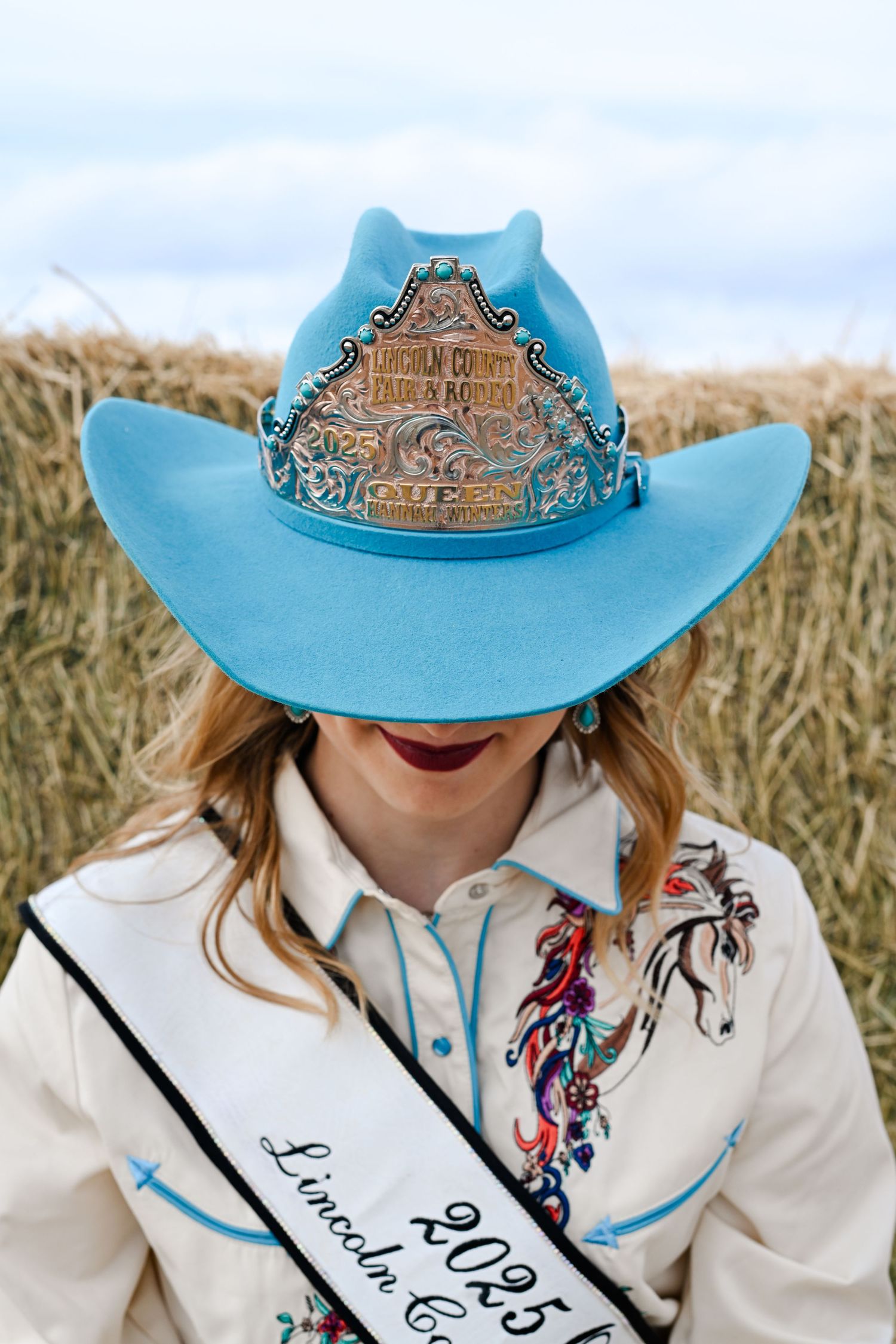 Light blue cowboy hat with ornate detailing worn with a white western shirt featuring colorful embroidery.