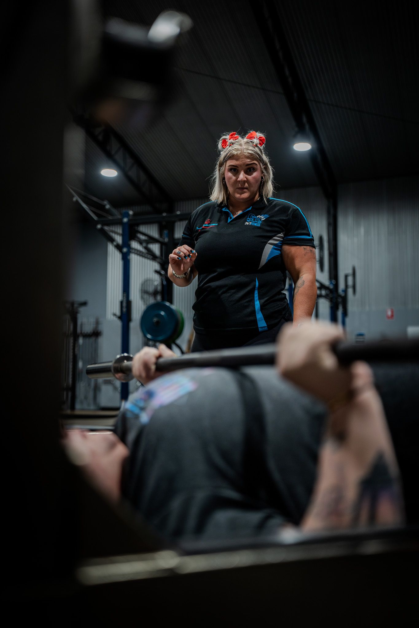 A dark and moody fitness scene showing spotters during a bench press exercise in a dimly lit gym.