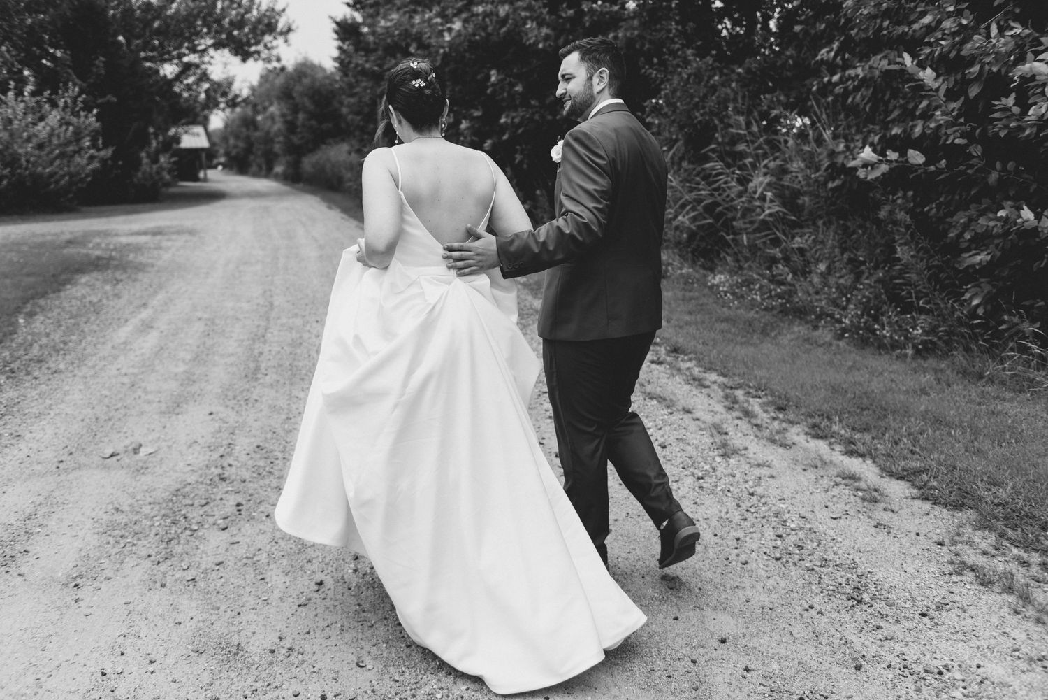 A couple walks together on a gravel path wearing formal wedding attire in black and white.